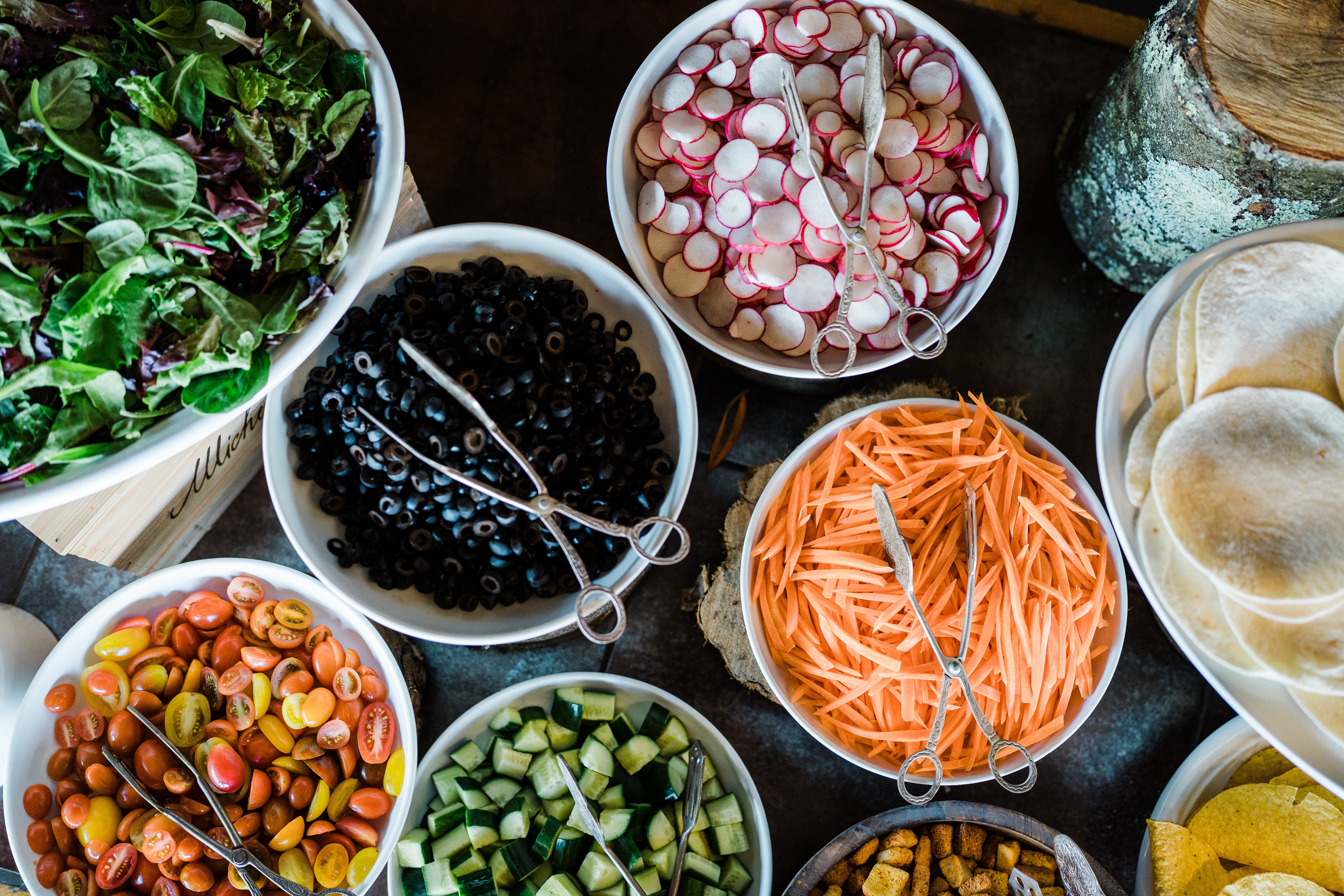 Fresh vegetables in bowls featuring tomatoes, olives, radish, carrots and cucumbers. 