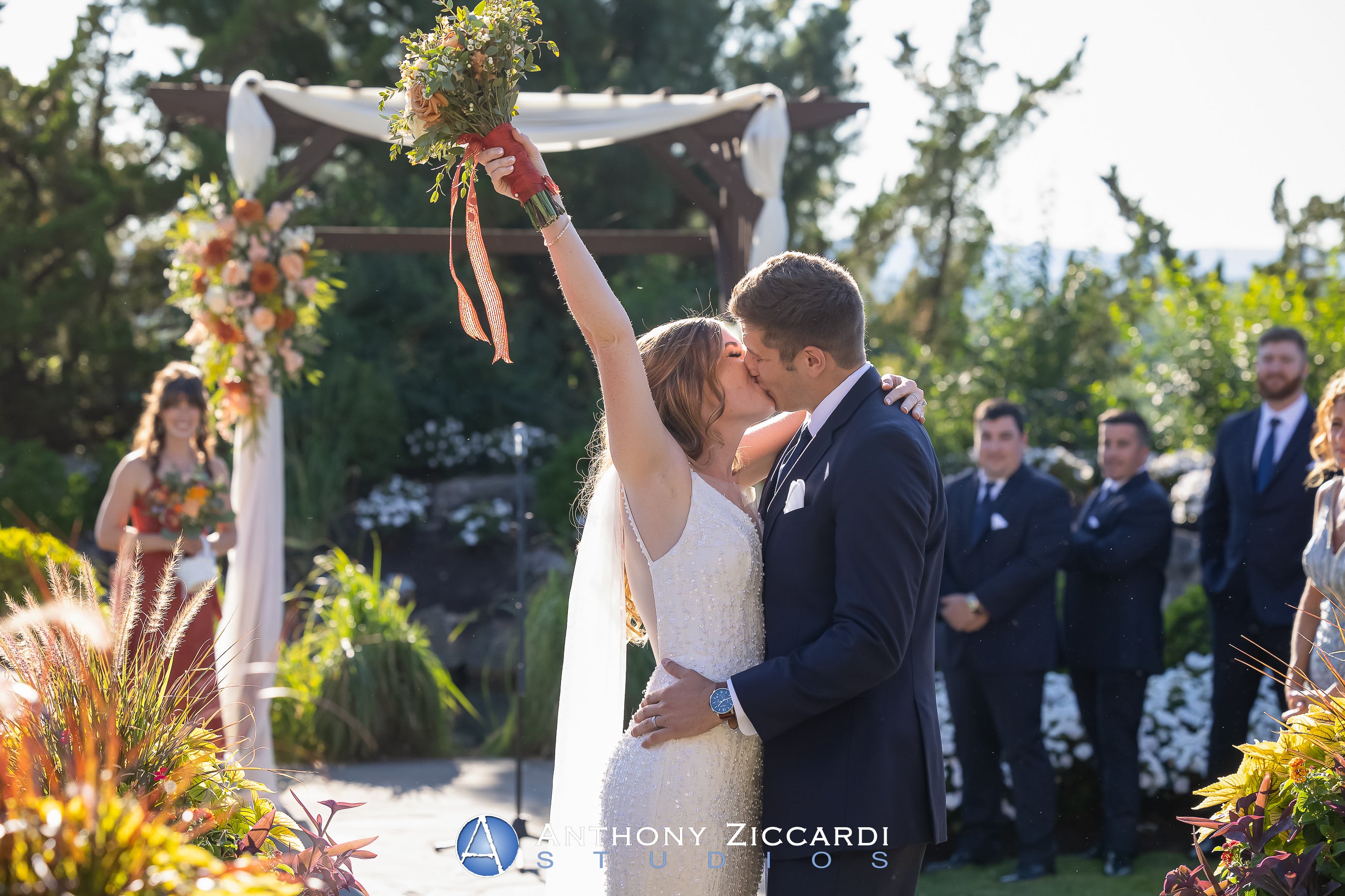 Bride and groom kiss under arch during their Bride walking down the aisle at Wedding Garden ceremony space at Crystal Springs Country Club. 