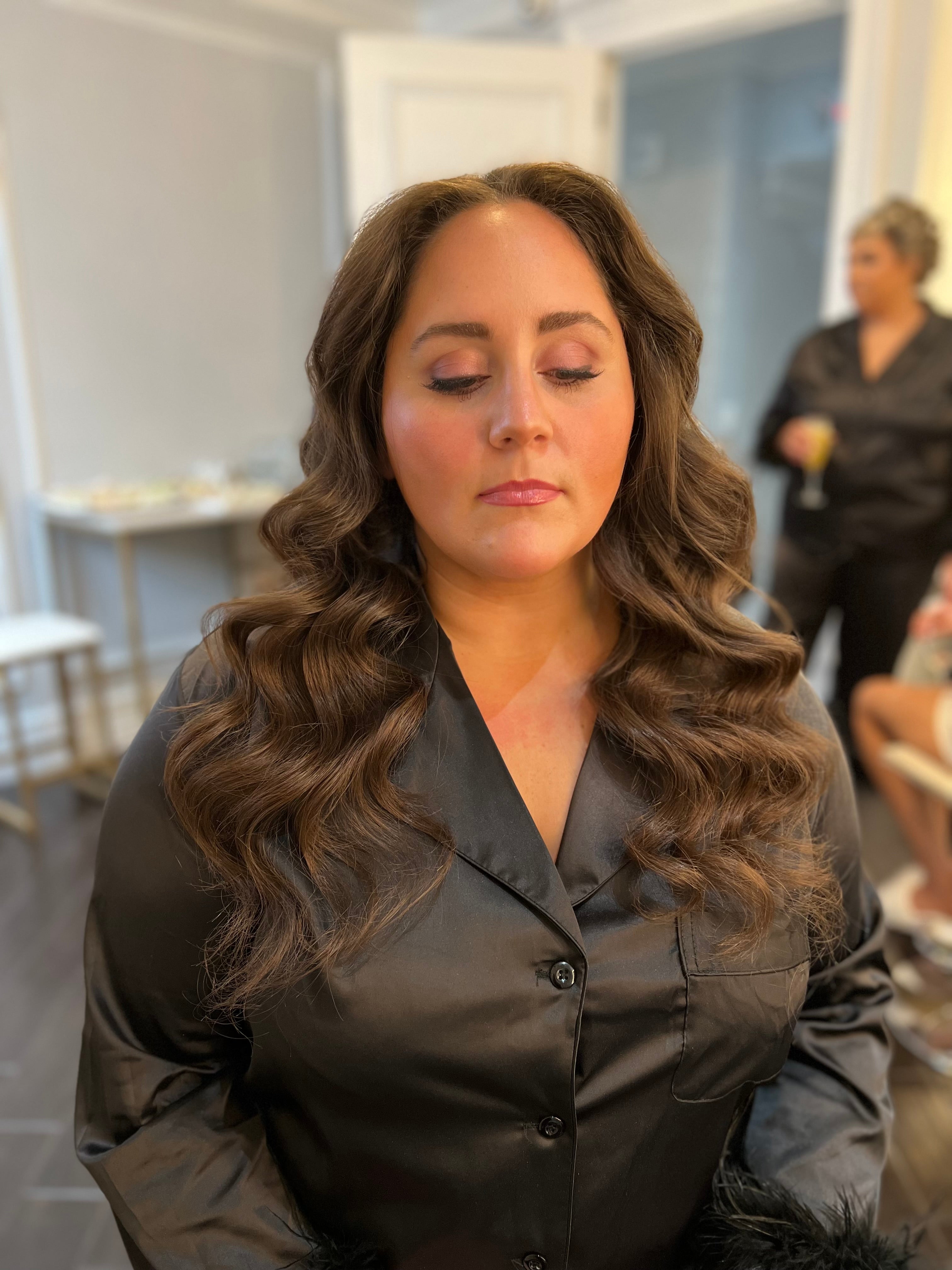 Woman sits with her eyes closed and her hair down styled wavy. 