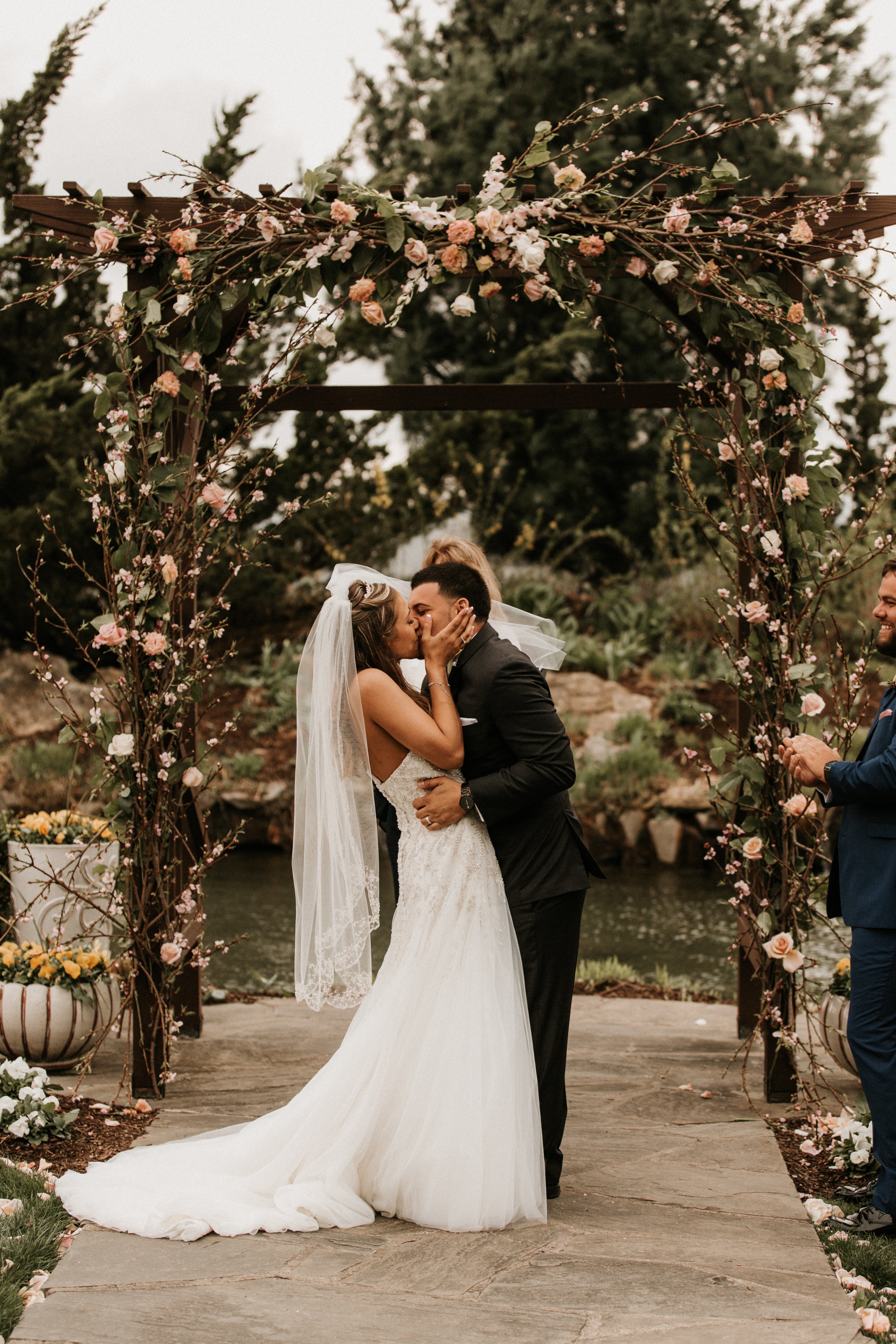 Bride and groom kiss under arch during their Bride walking down the aisle at Wedding Garden ceremony space at Crystal Springs Country Club. 