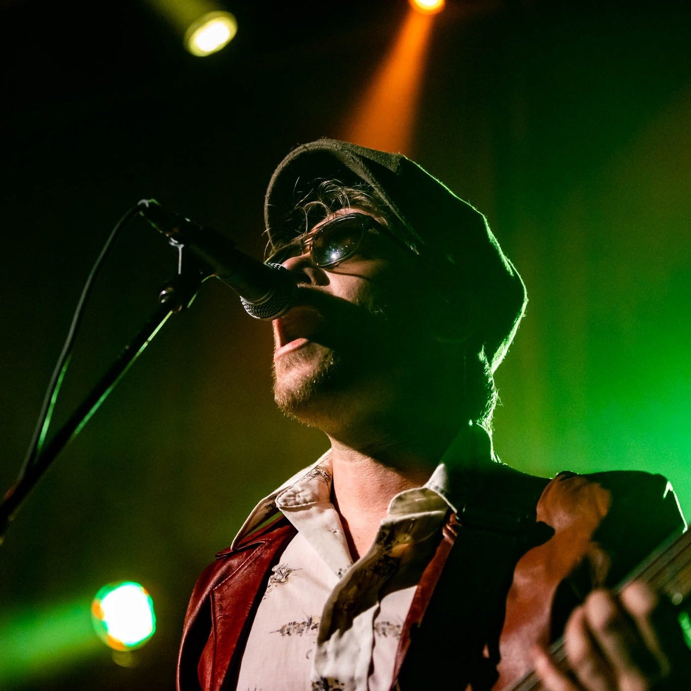 Man wearing hat and sunglasses singing into microphone