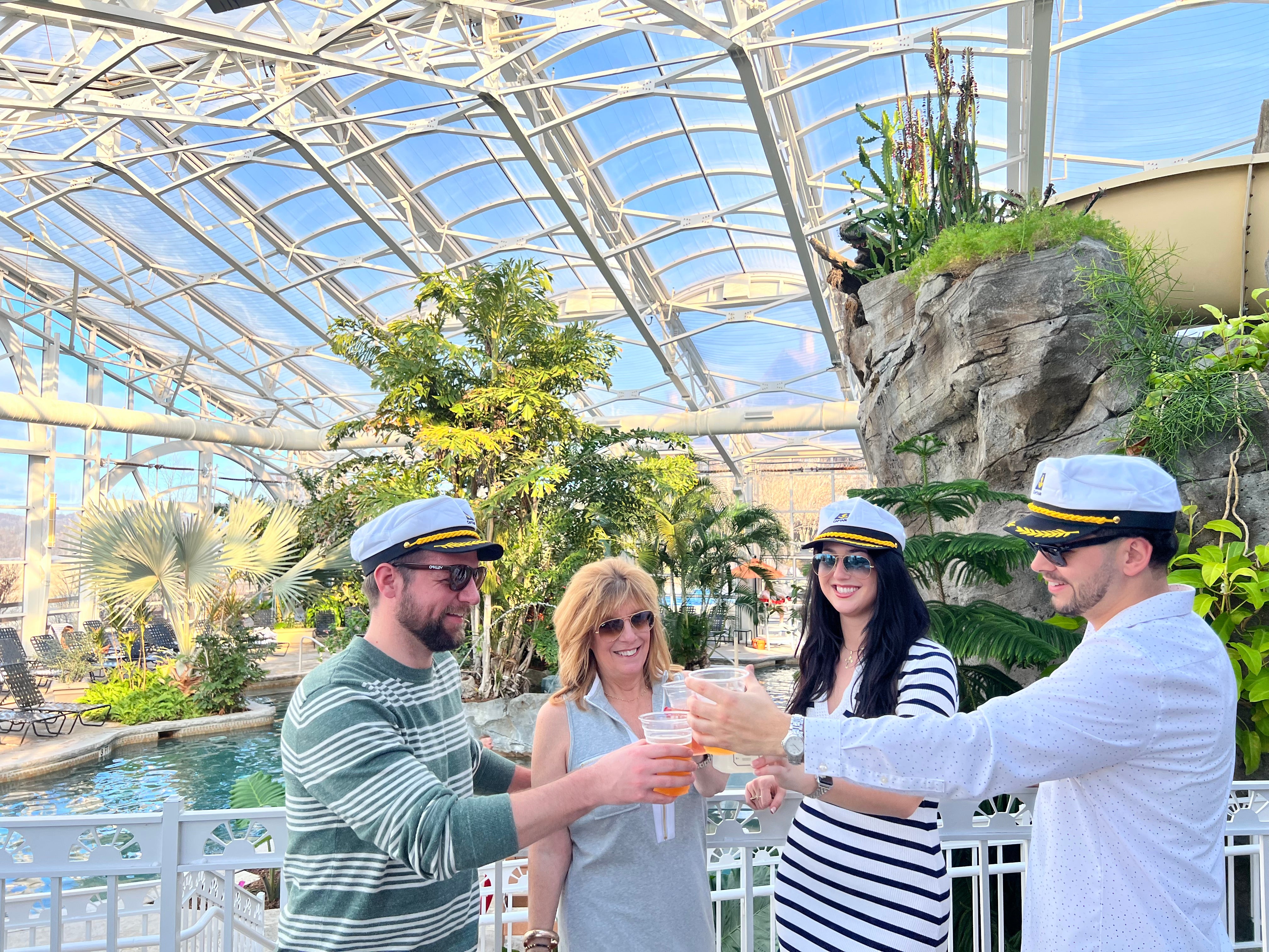 Four people stand with captain hats in Biosphere pool cheersing their drinks.