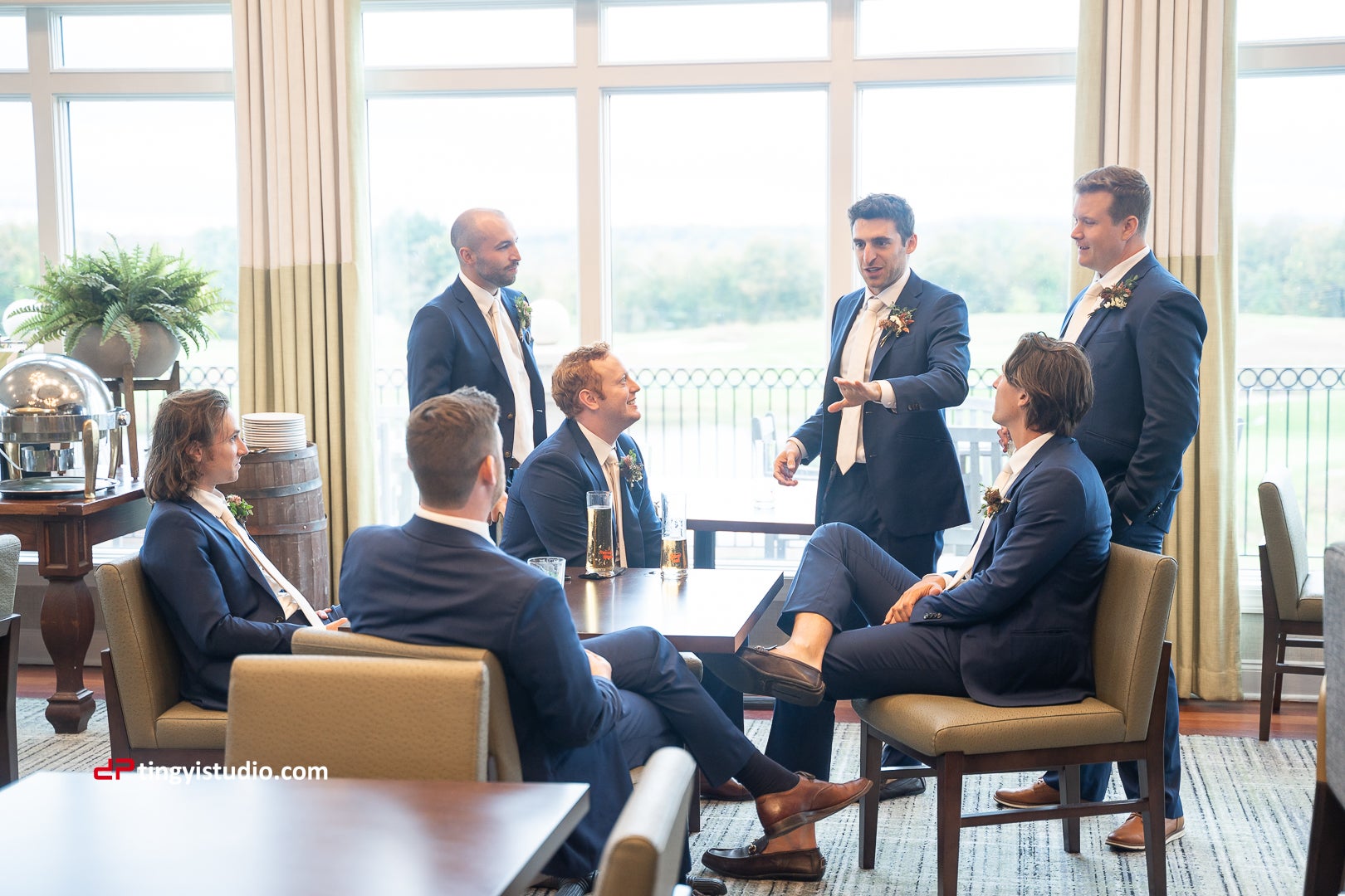 Groomsmen sitting around a table talking in navy blue suits.