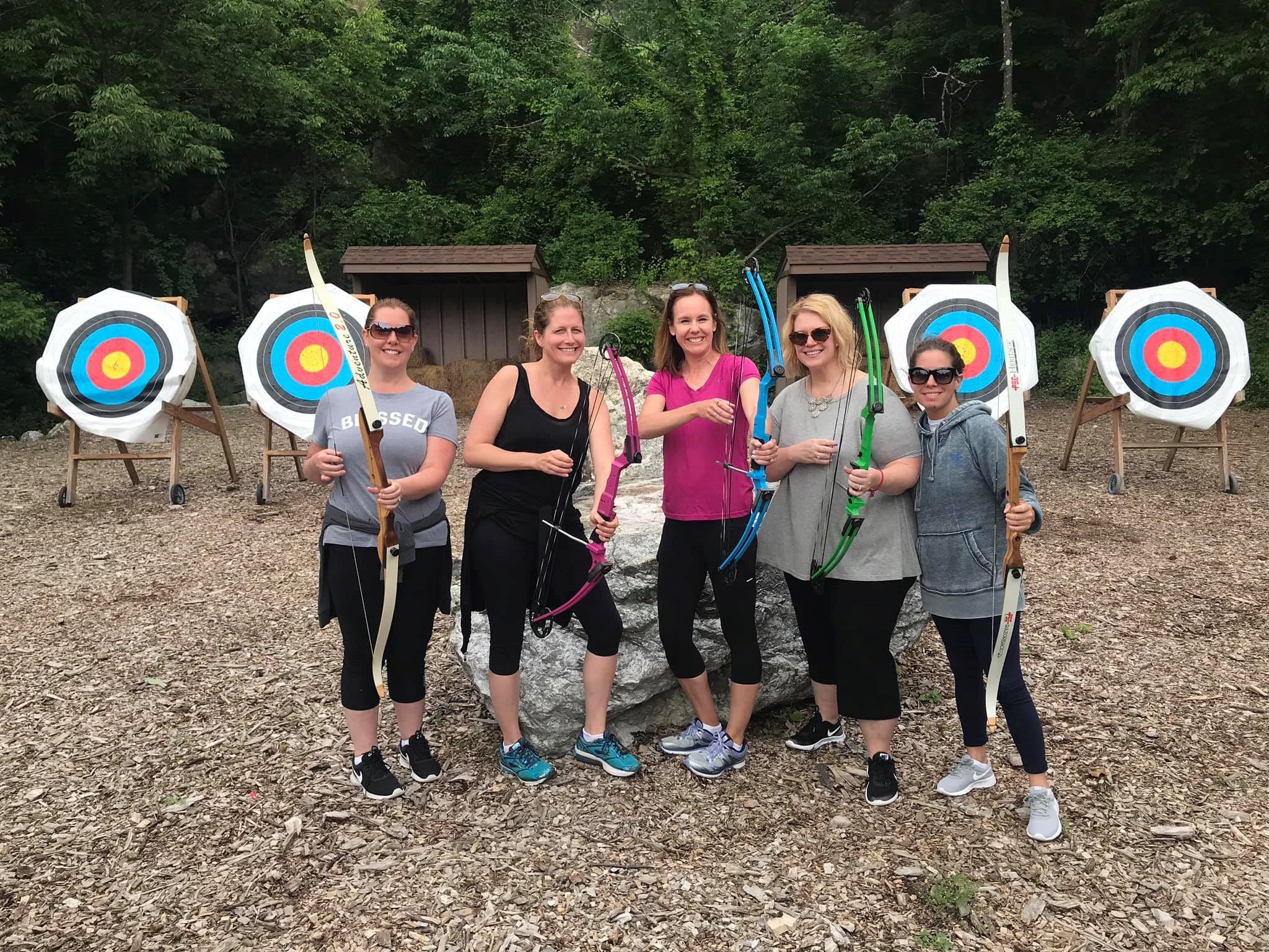 Five girlfriends holding bows at archery range. 