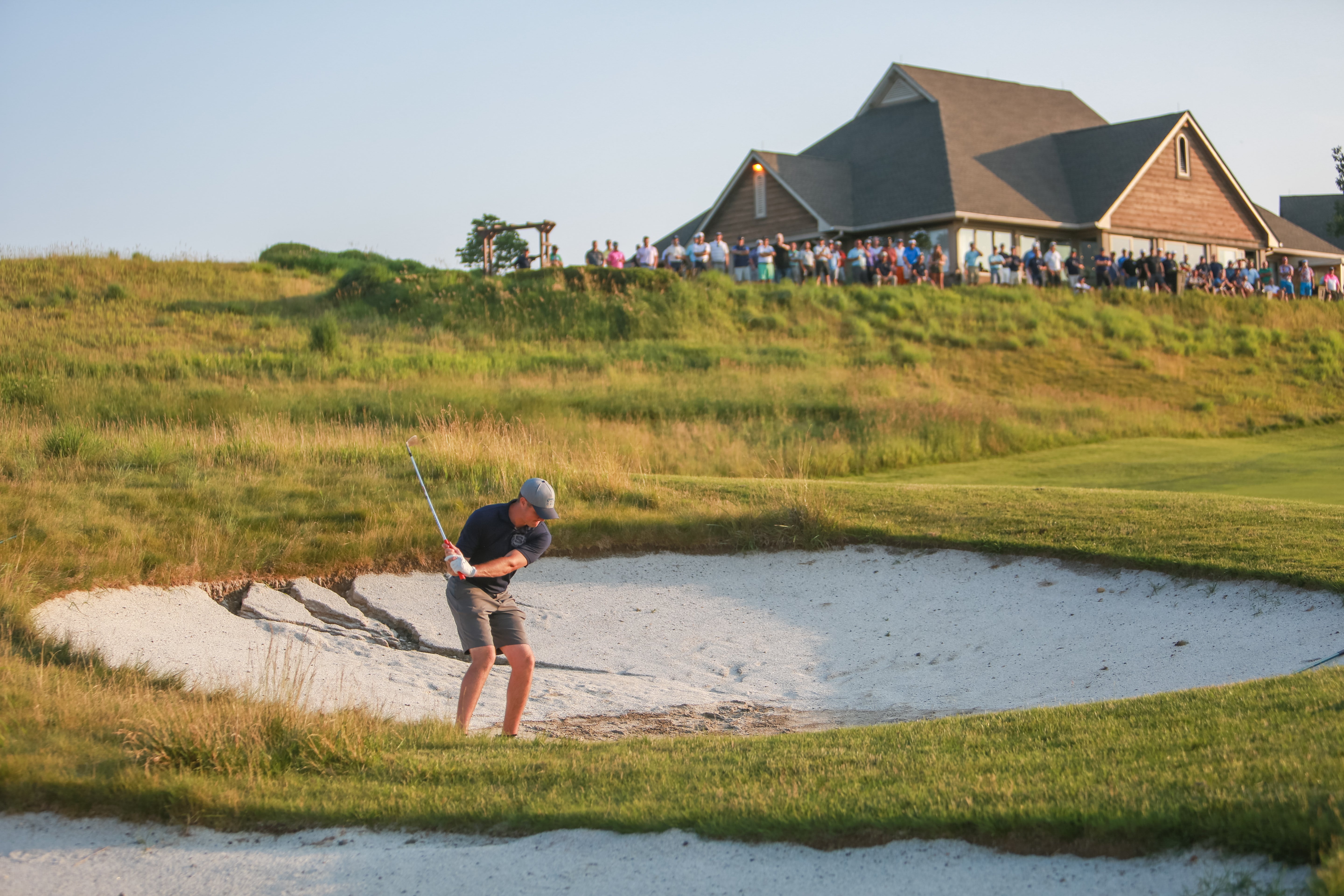 Man chipping golf ball out of the sand. 