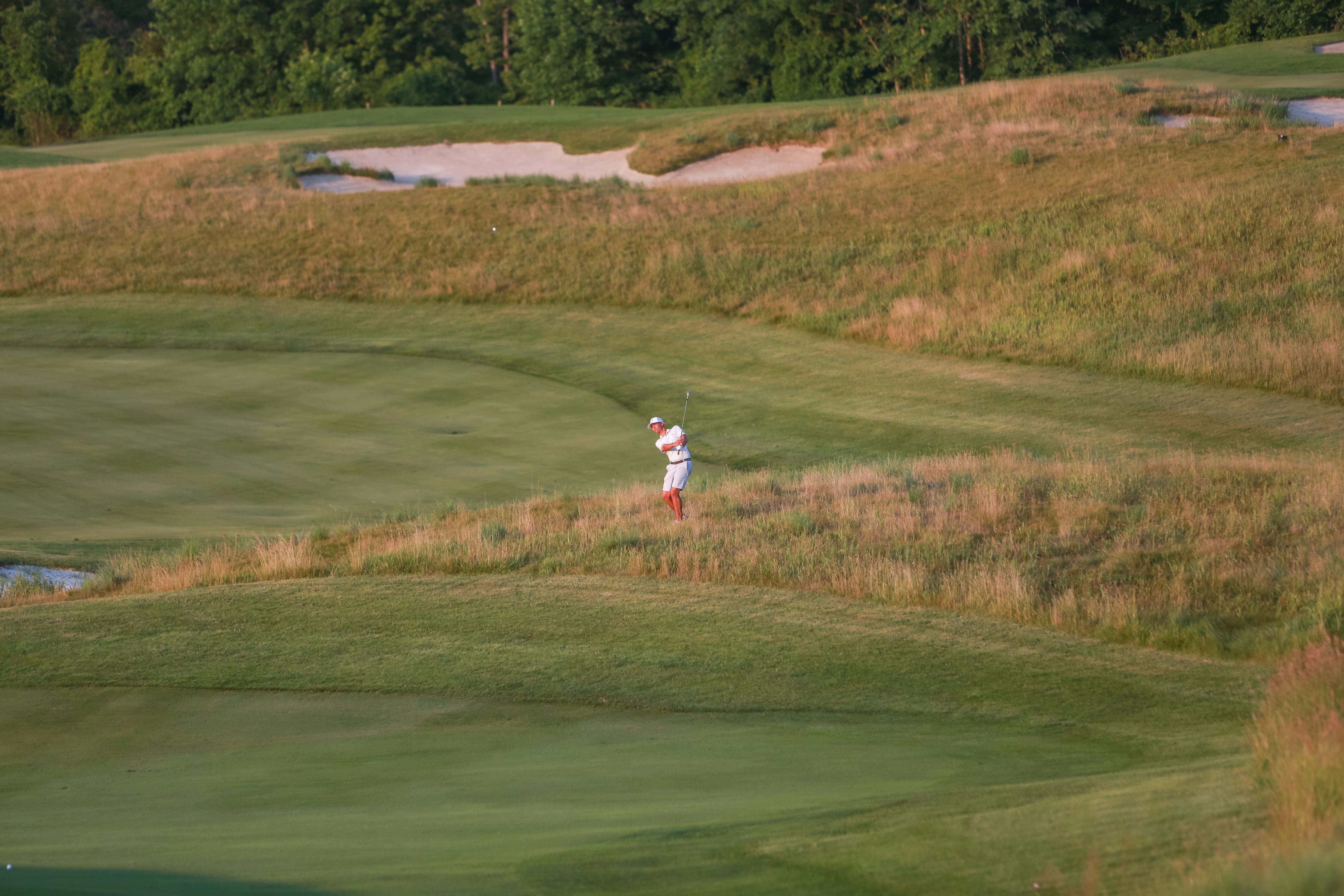 Man swinging golf club on course. 