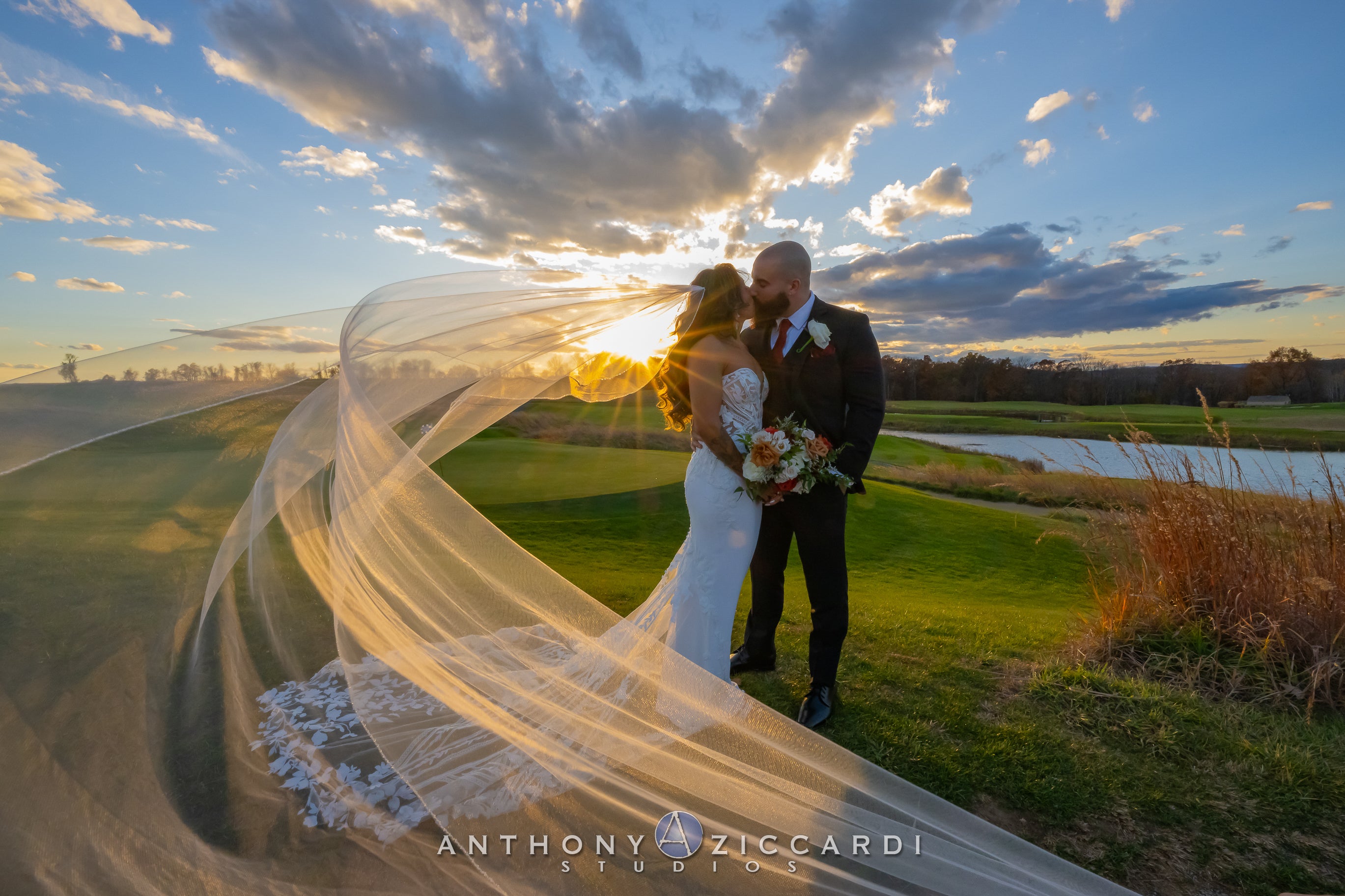 Bride and groom stand side by side as bride's veil flows through the wind.
