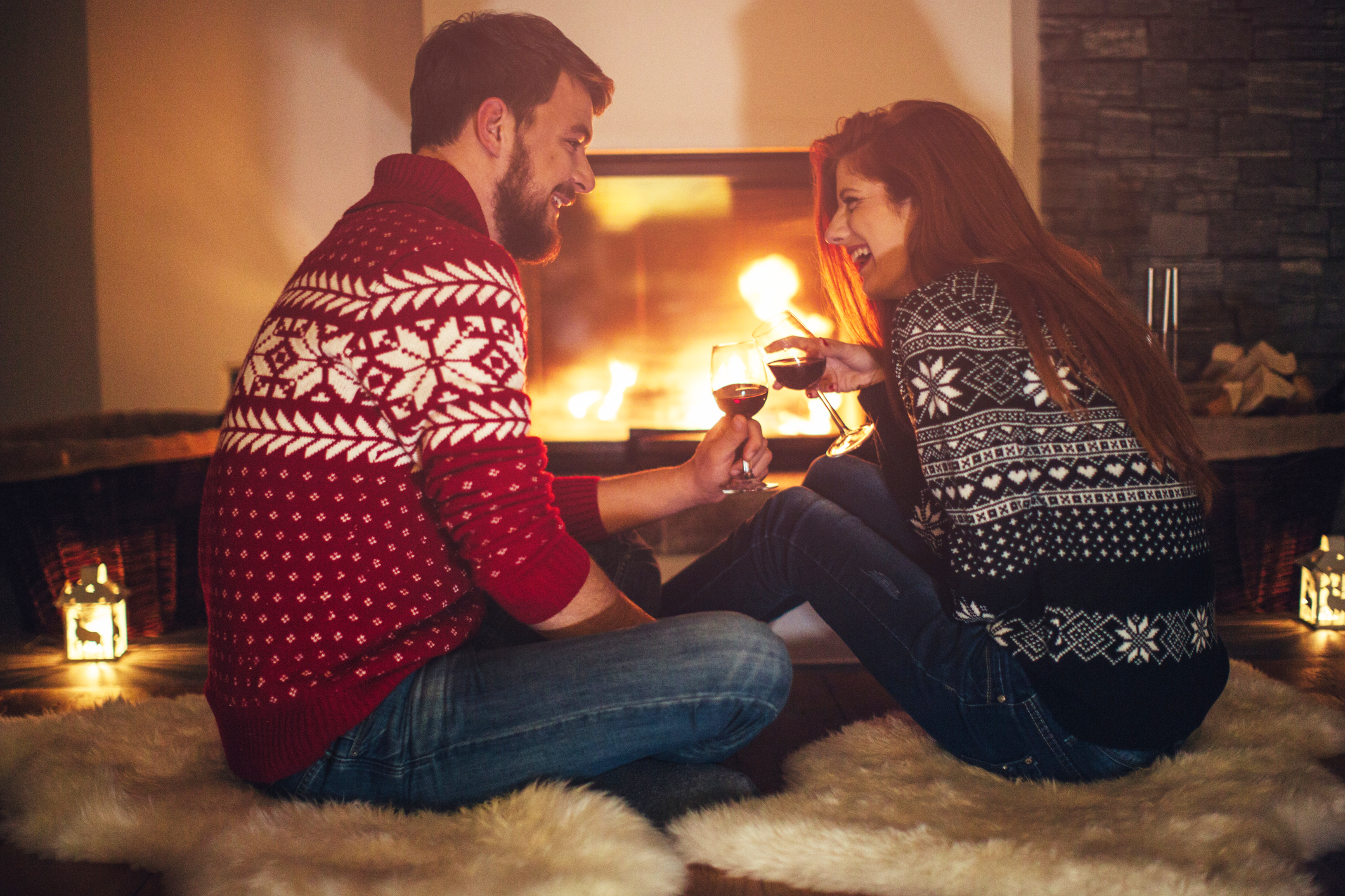 Couple sitting in front of fireplace drinking wine.