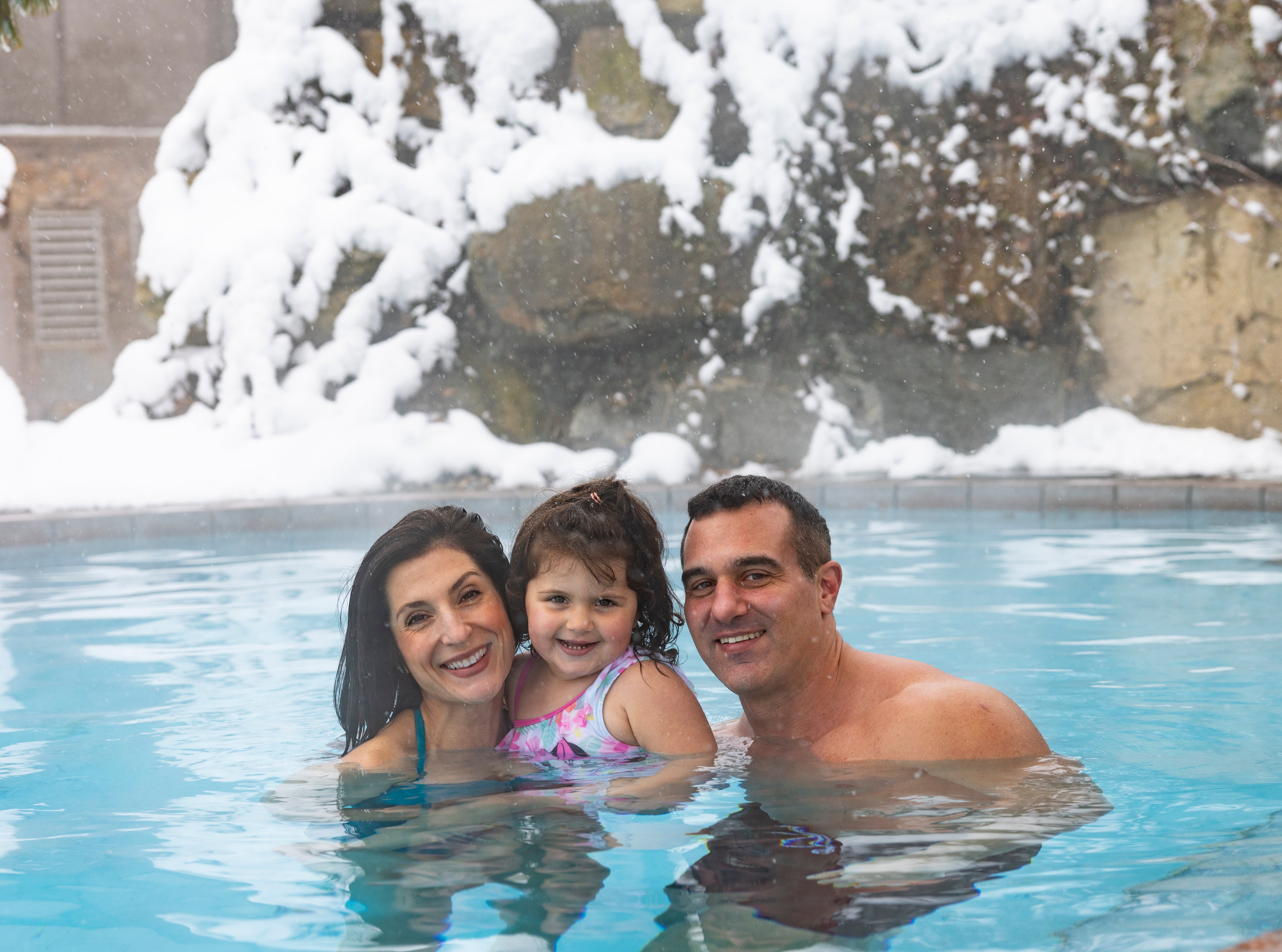 Mom and dad hold their daughter in outdoor snow pool.