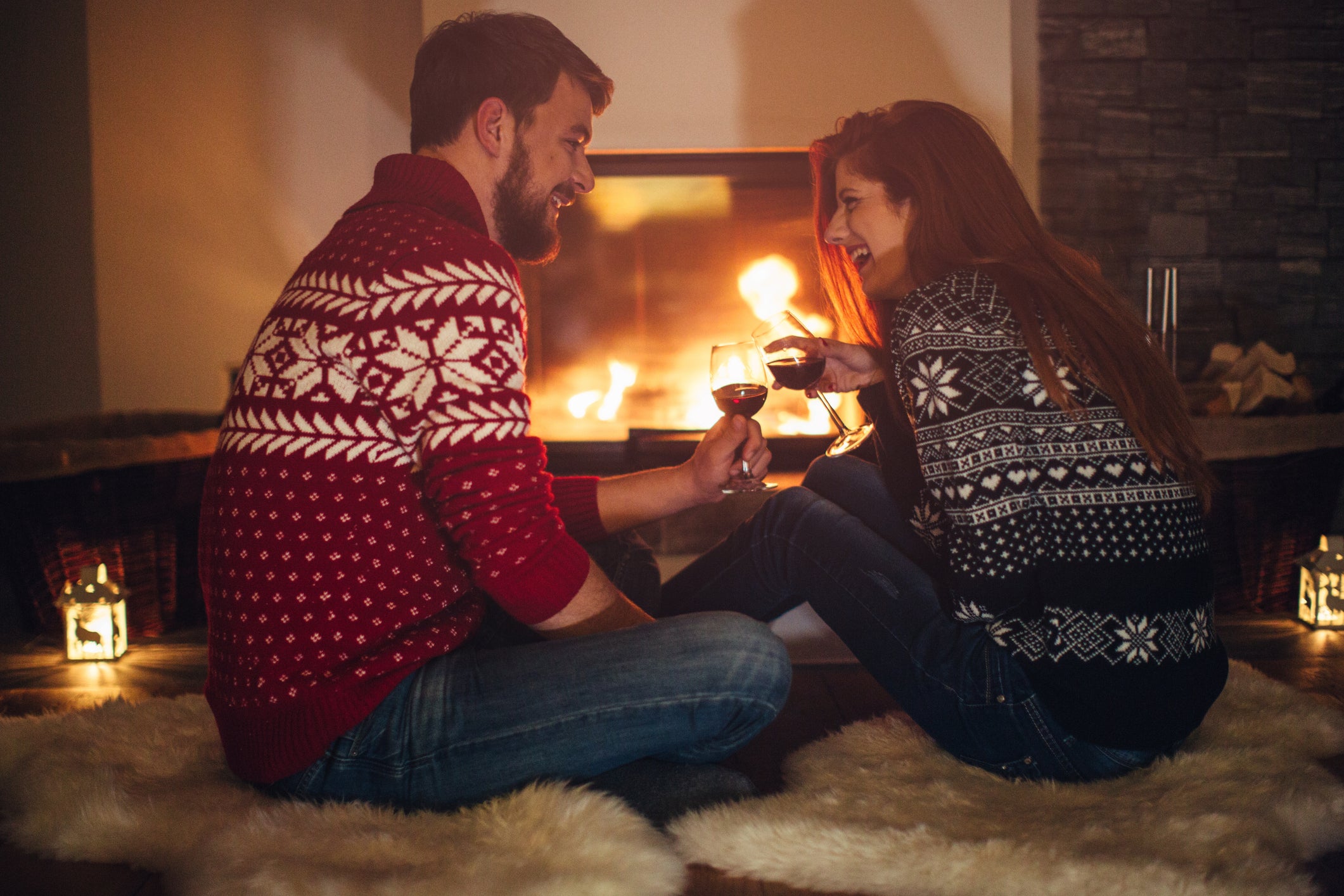 Couple sitting in front of fireplace drinking wine.