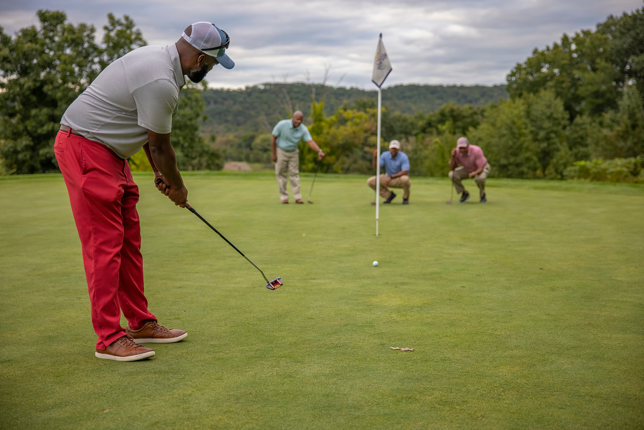 Golfers participate in a group outing on a putting green at Crystal Springs Resort, with wooded hills in the background.