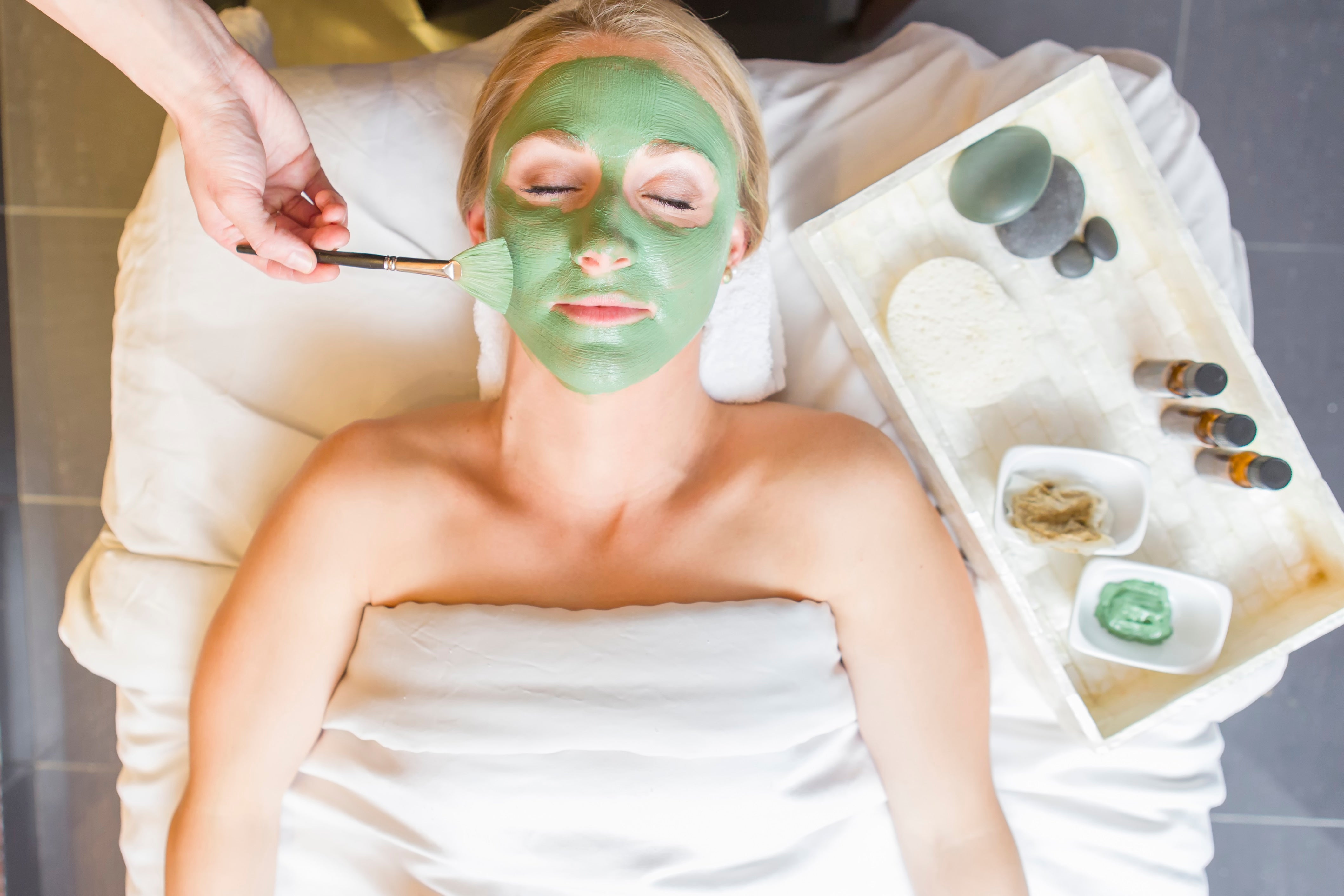 Woman laying on spa table with green mask on her face.
