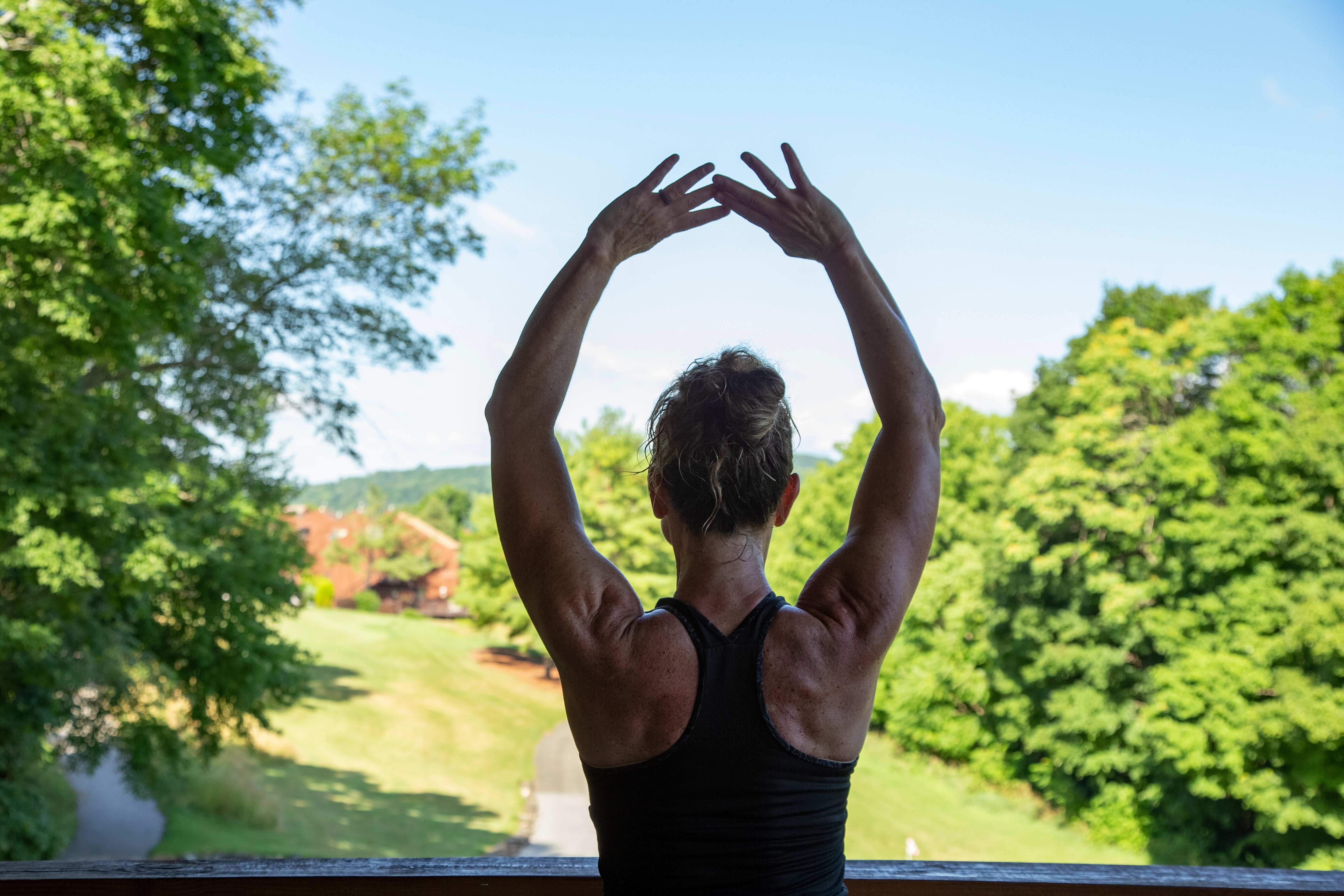 Woman with her arms up above her head facing away.