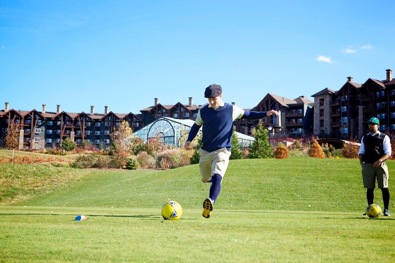 Guy wearing hat kicking a foot golf ball