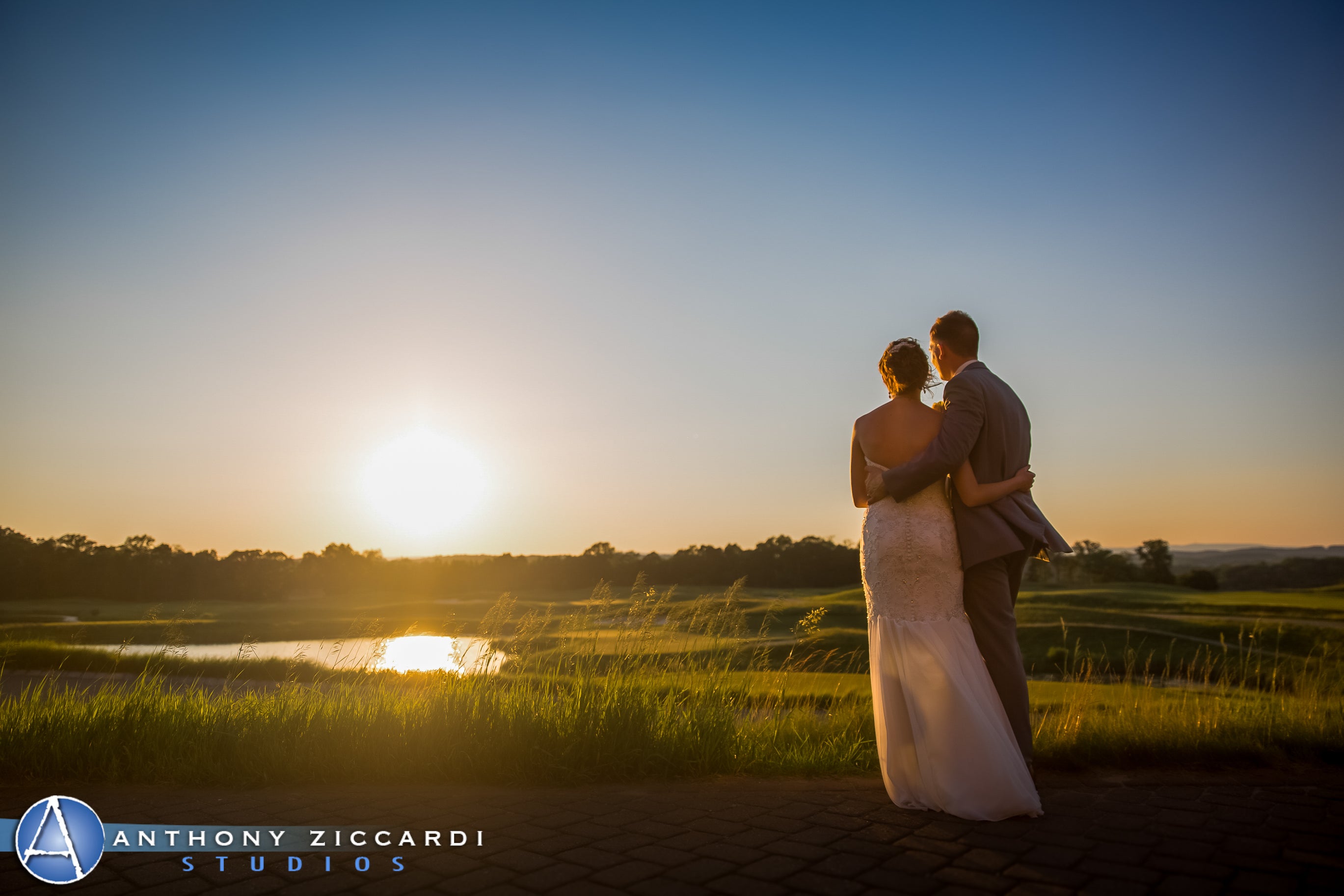 Bride and groom arms around each other looking into the sun