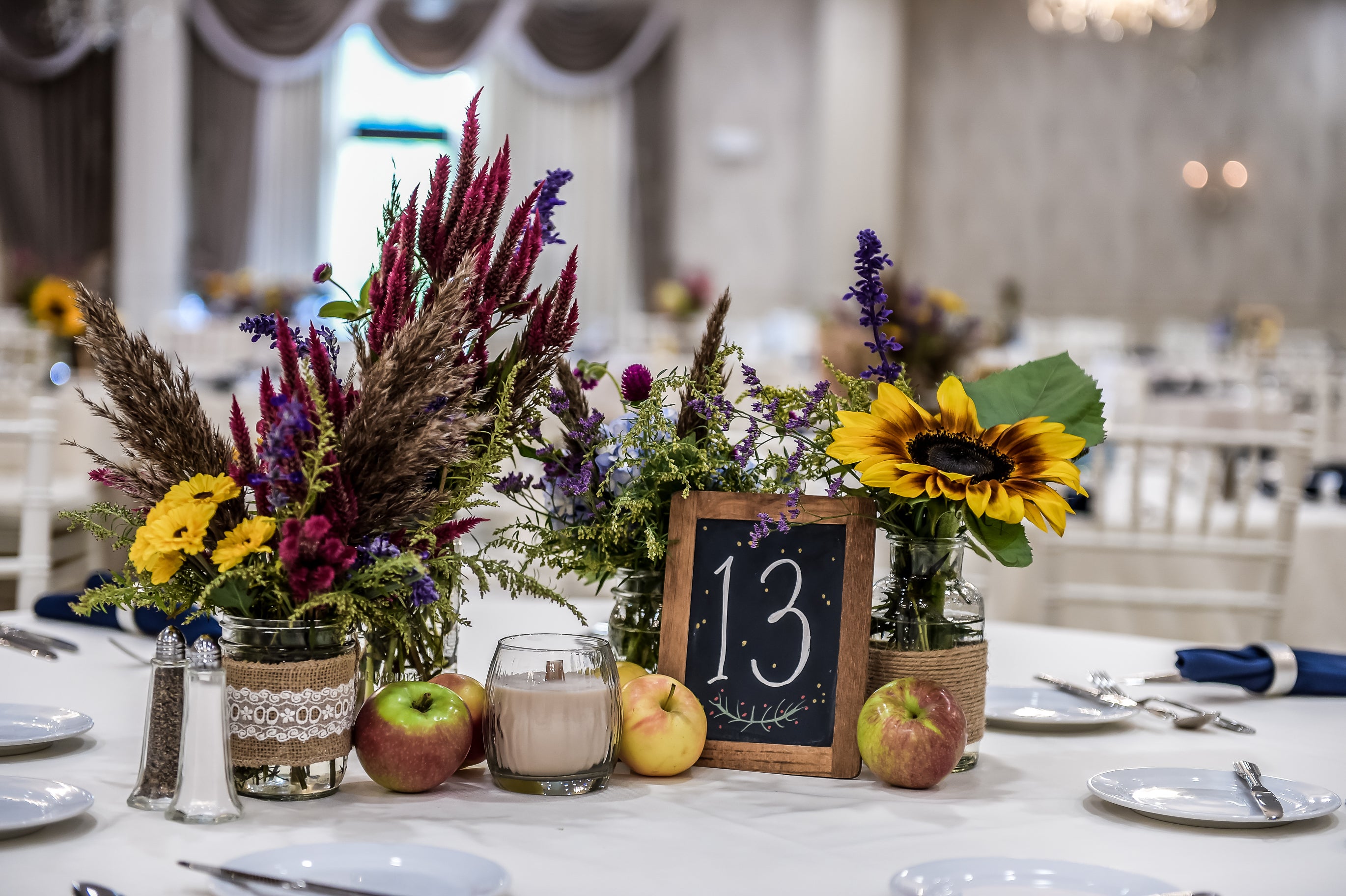 Centerpieces of wedding reception featuring apples, yellow flowers and table number 13. 