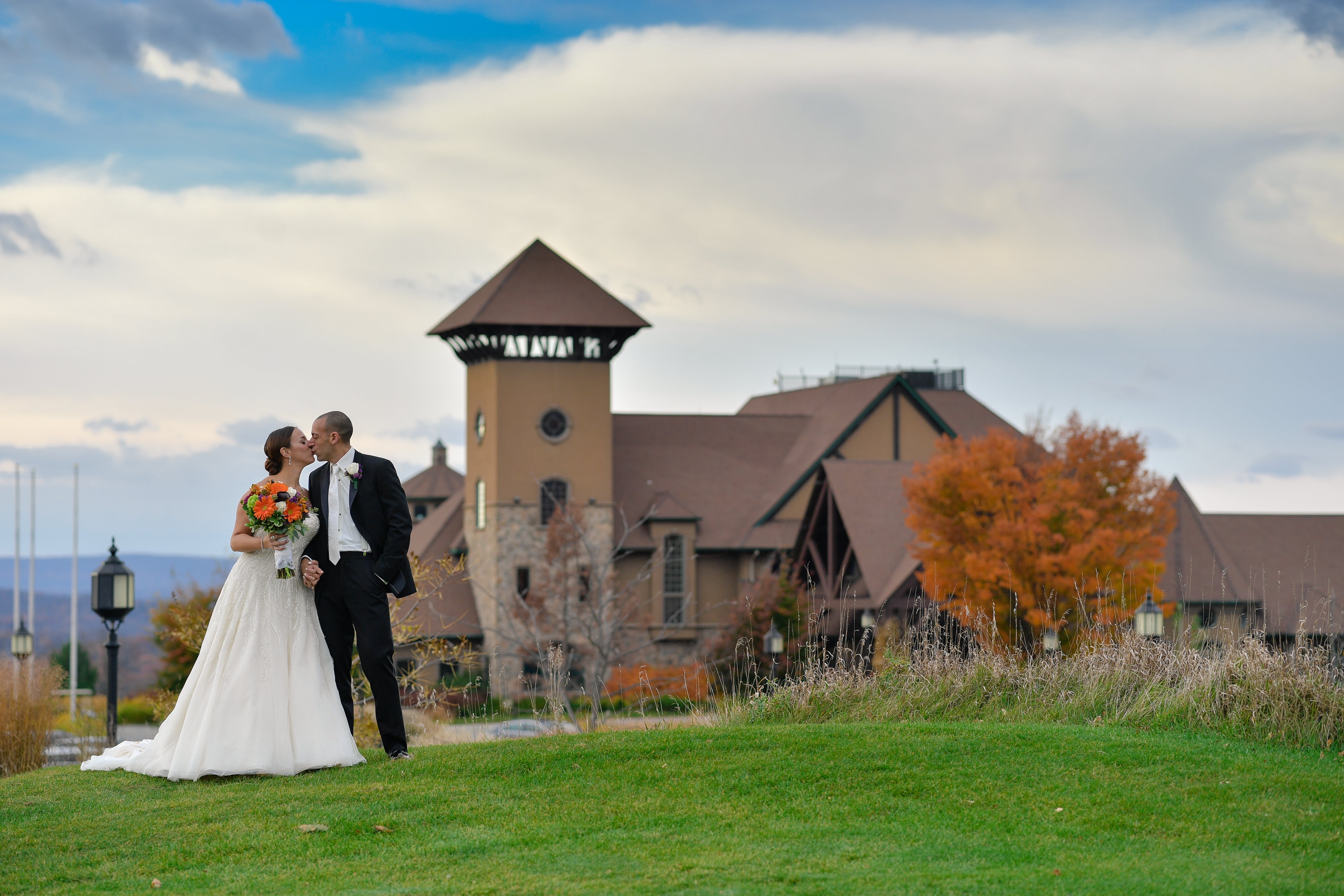 Bride and groom kissing in front of fall foliage and Crystal Springs Clubhouse
