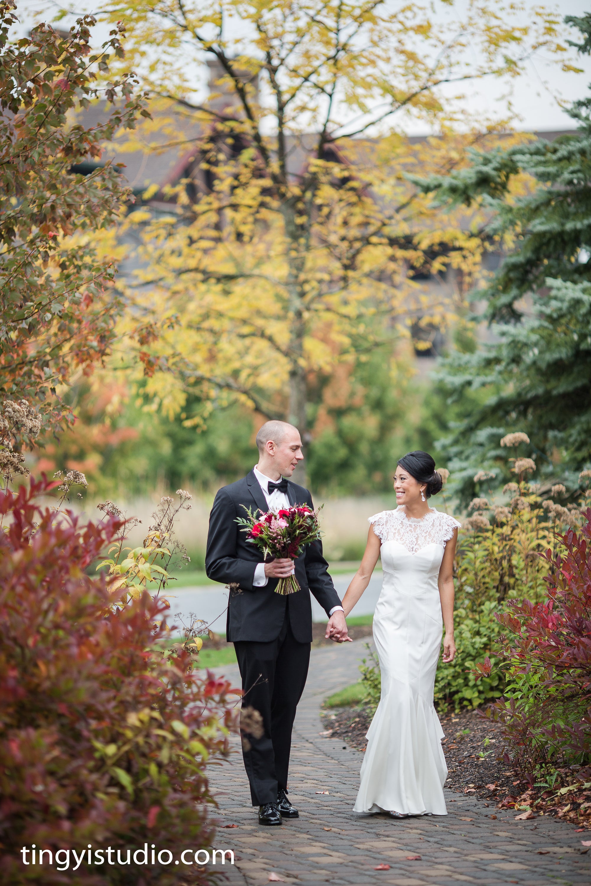 Bride and groom holding hands walking through fall path.