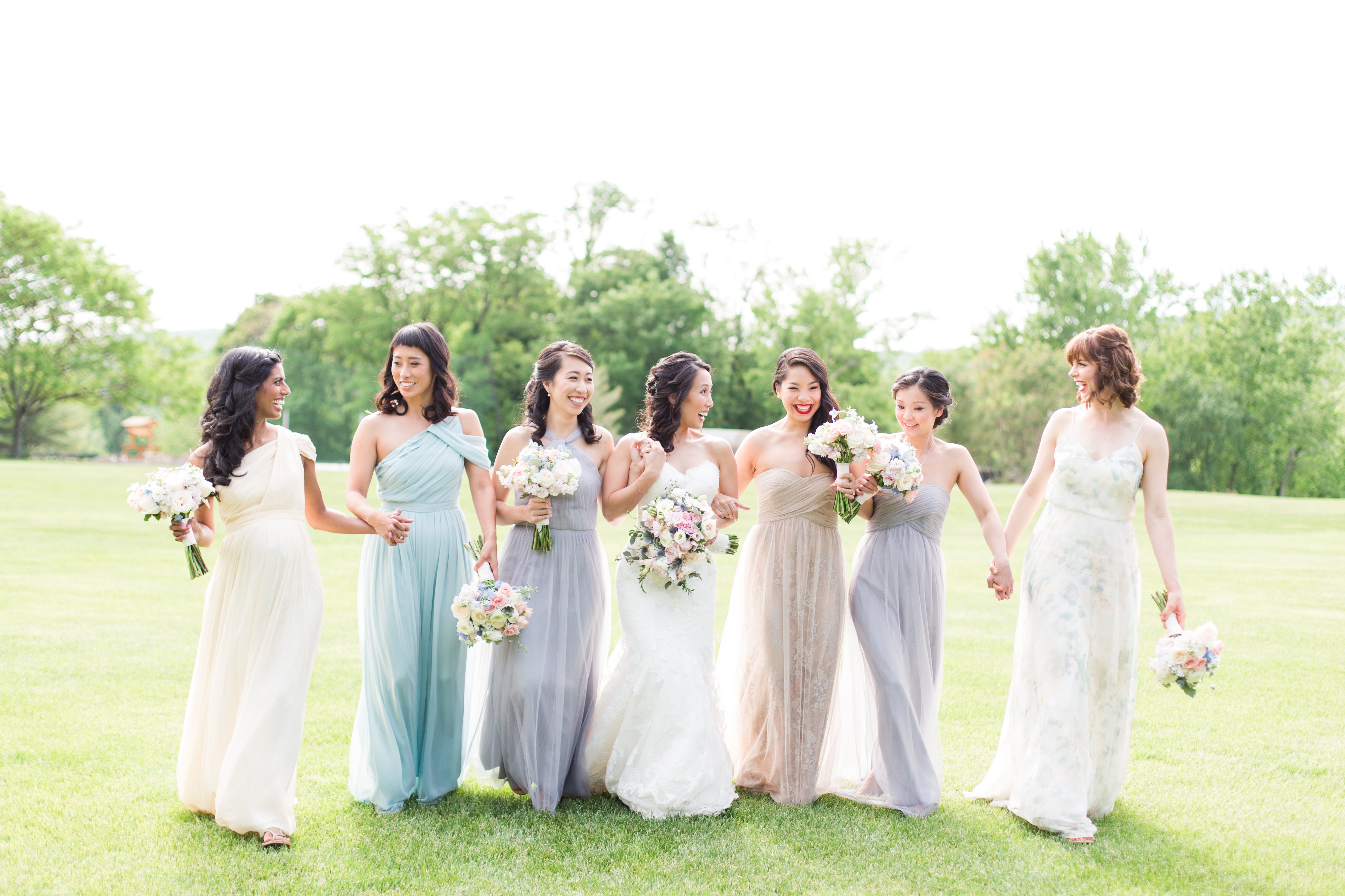 Bridesmaids and bride walk through grass field.