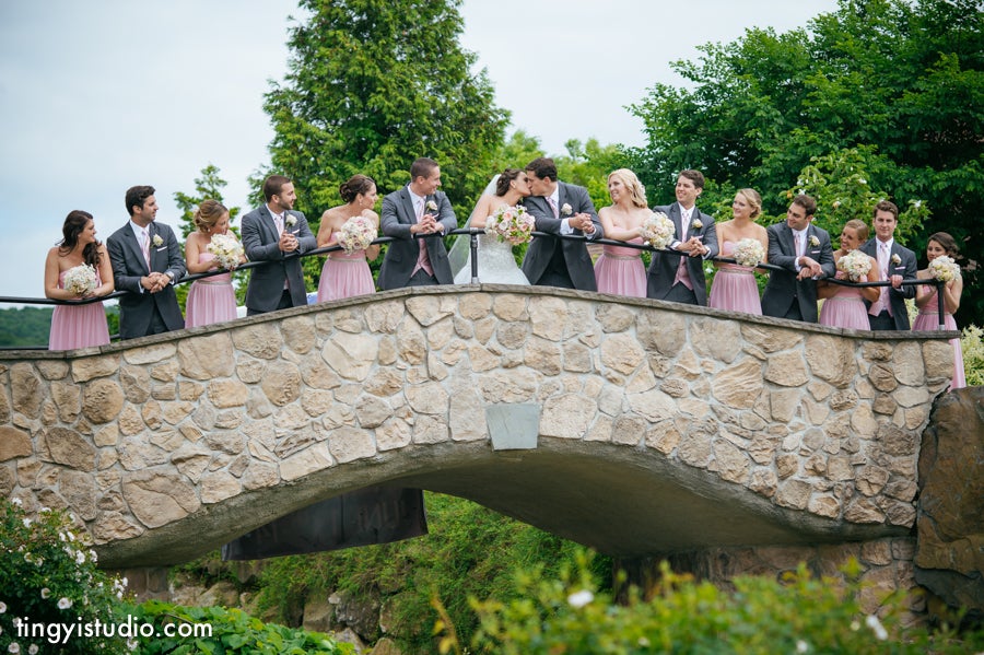 Wedding party stands on stone bridge.