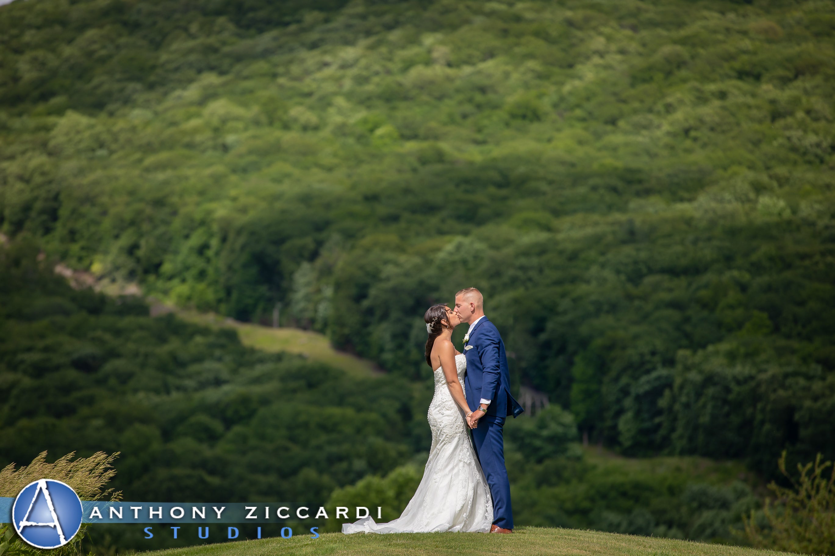 Bride and groom kiss in front of green mountains in background.