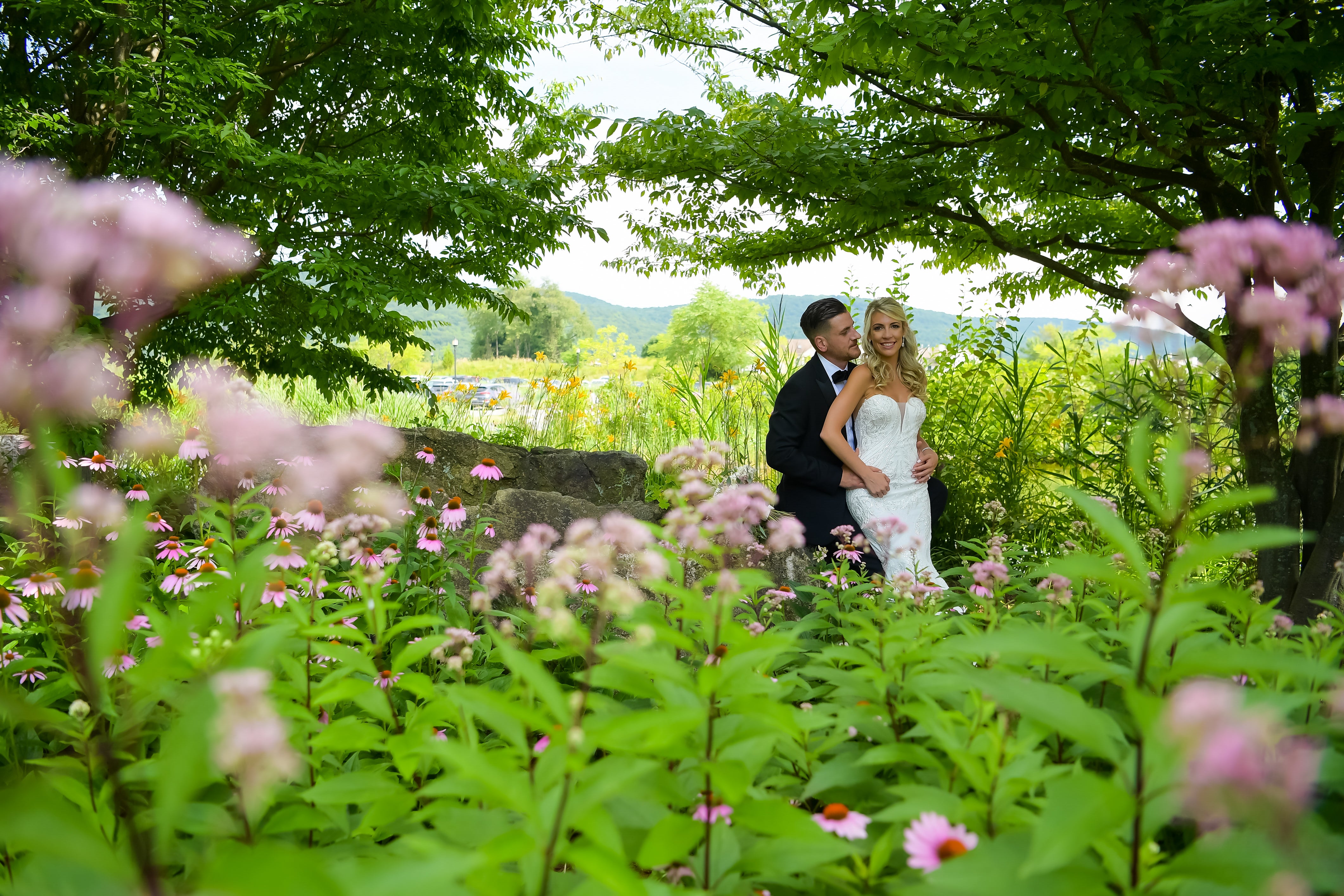 Bride and groom stand between green and pink florals.