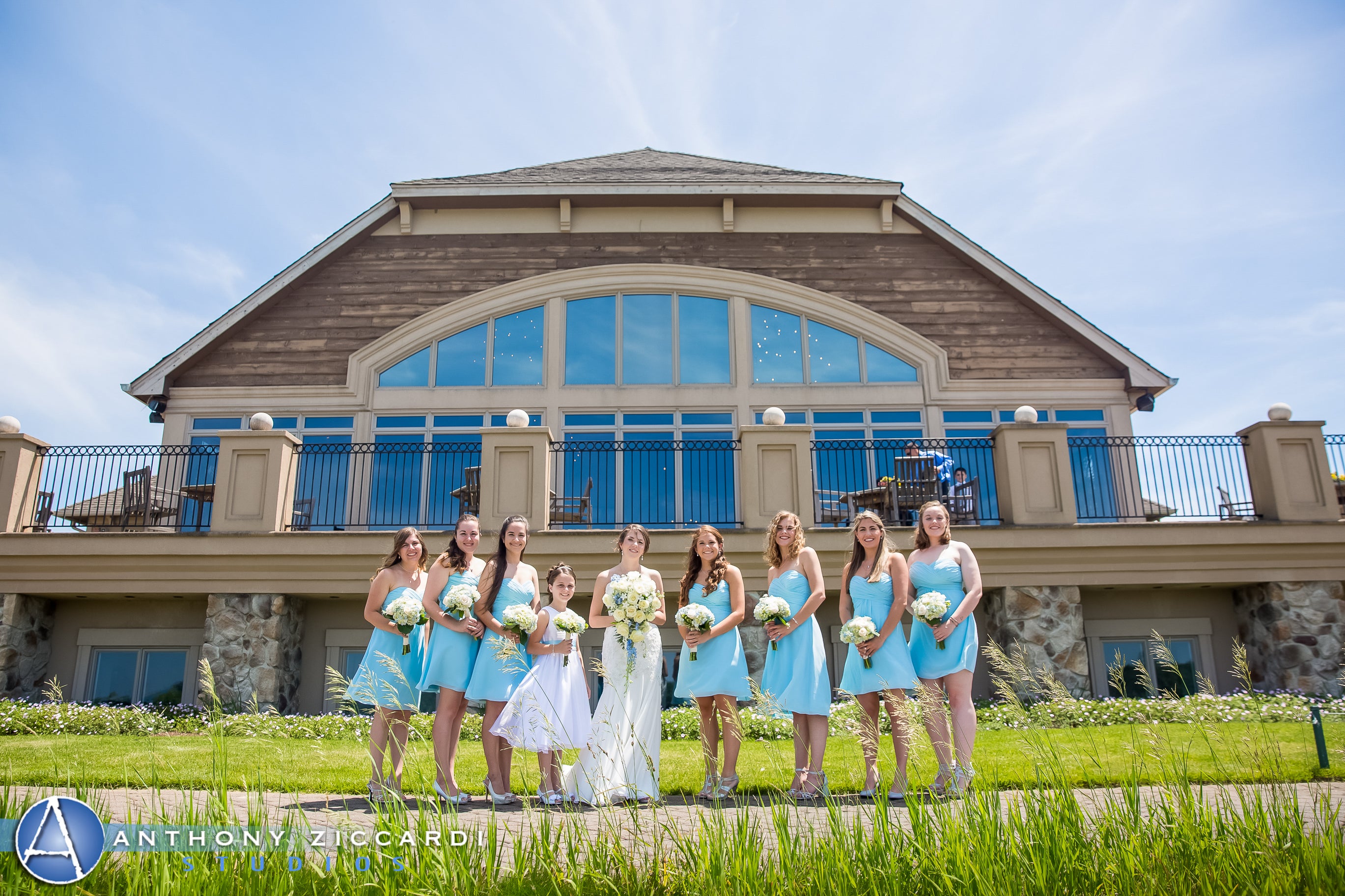 Bridesmaids, wearing short light blue dresses, stand with bride in front of Ballyowen Golf Club.