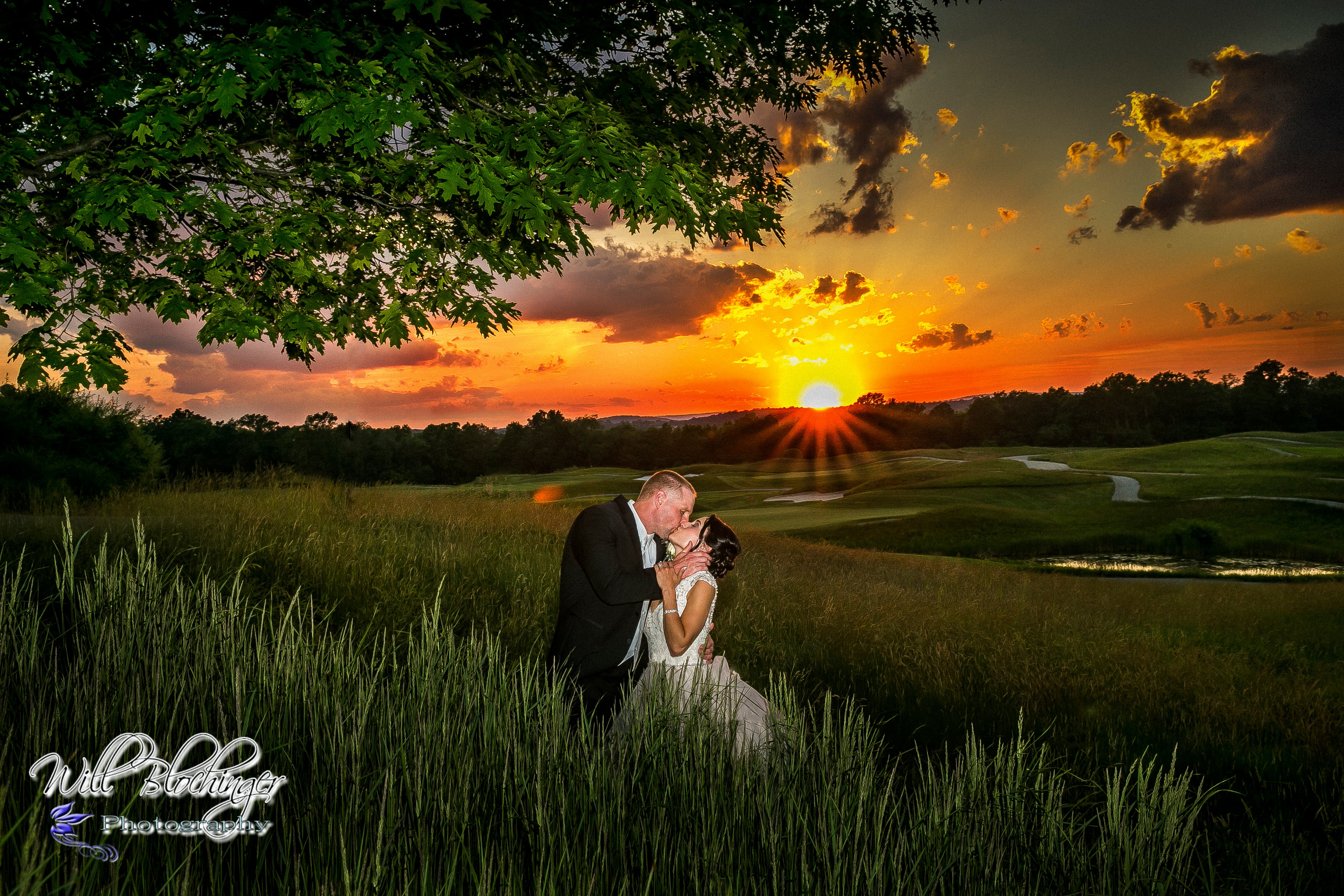 Bride and groom kiss with orange sunset behind them.
