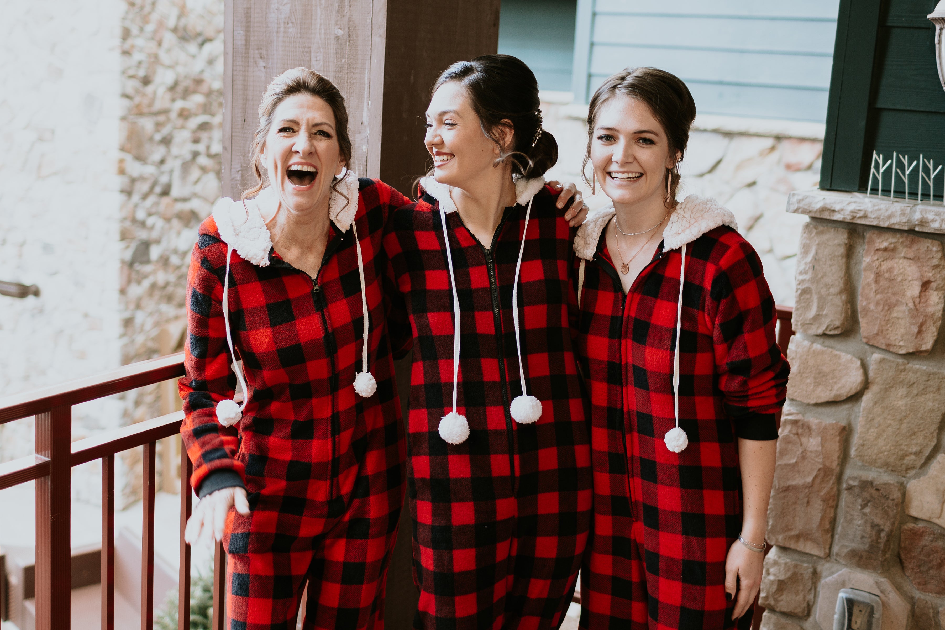 Three women stand together wearing flannel onesies.