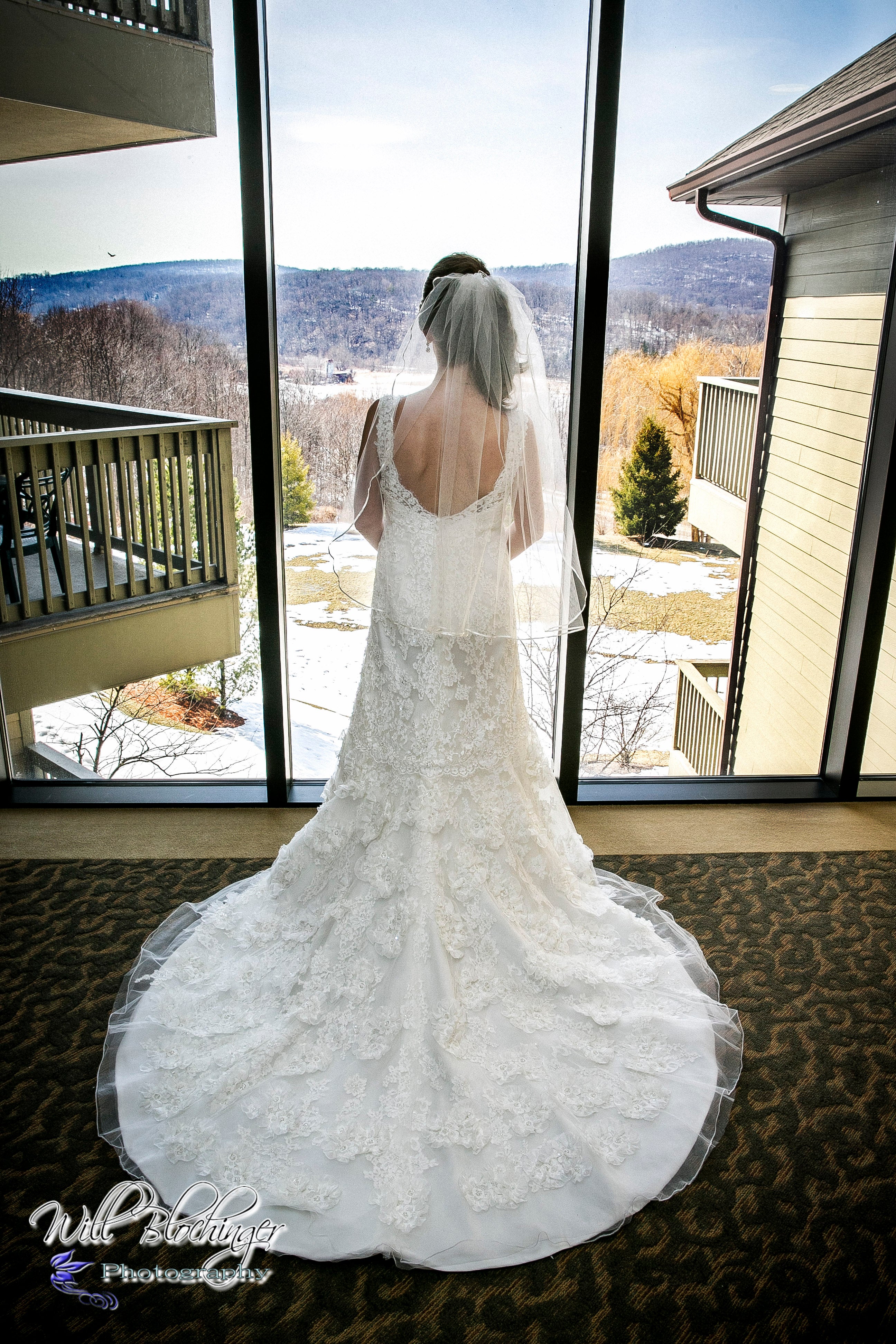 Bride looks out large window to see mountain range in distance.