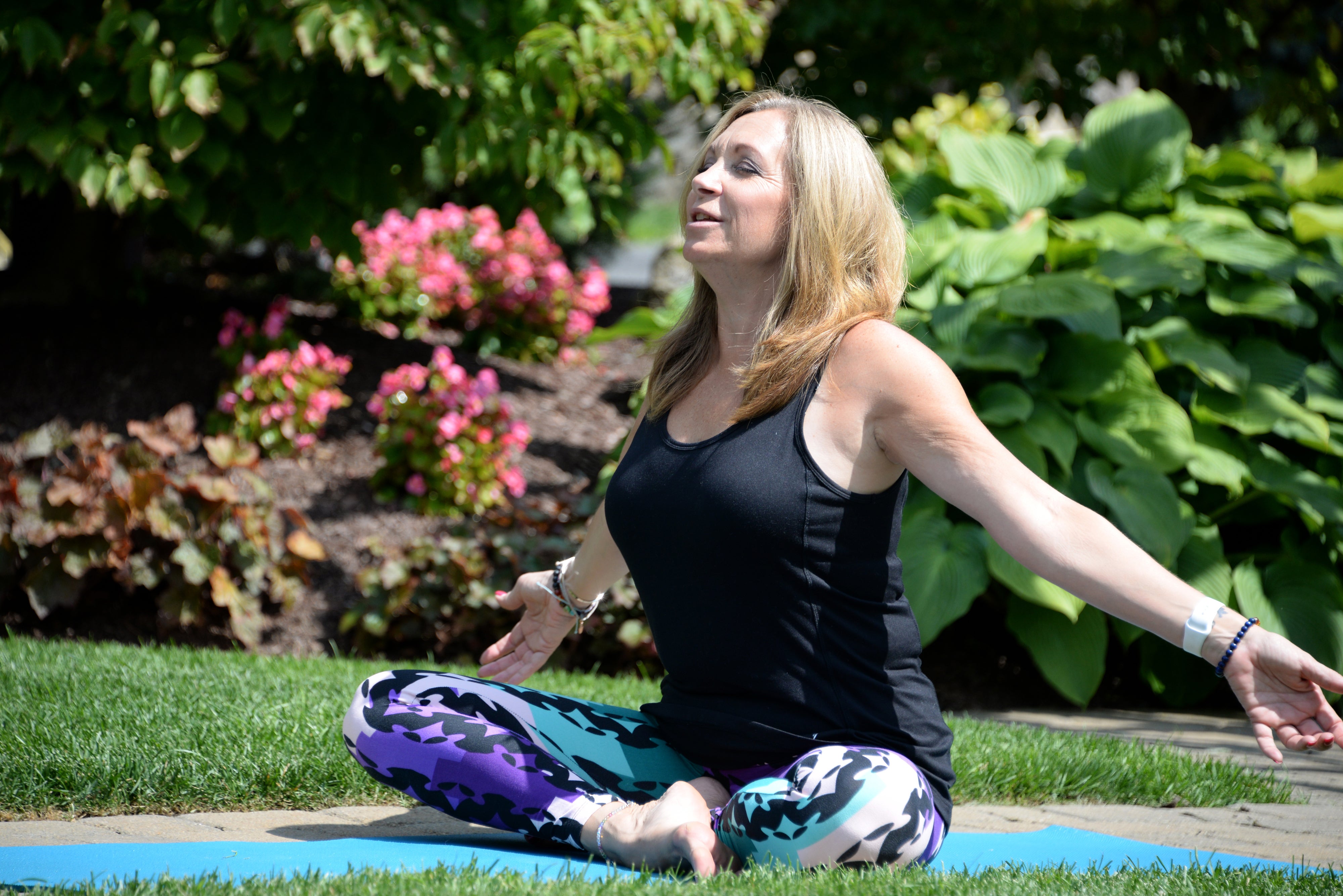 Woman sitting outside doing yoga with her arms stretched out wide