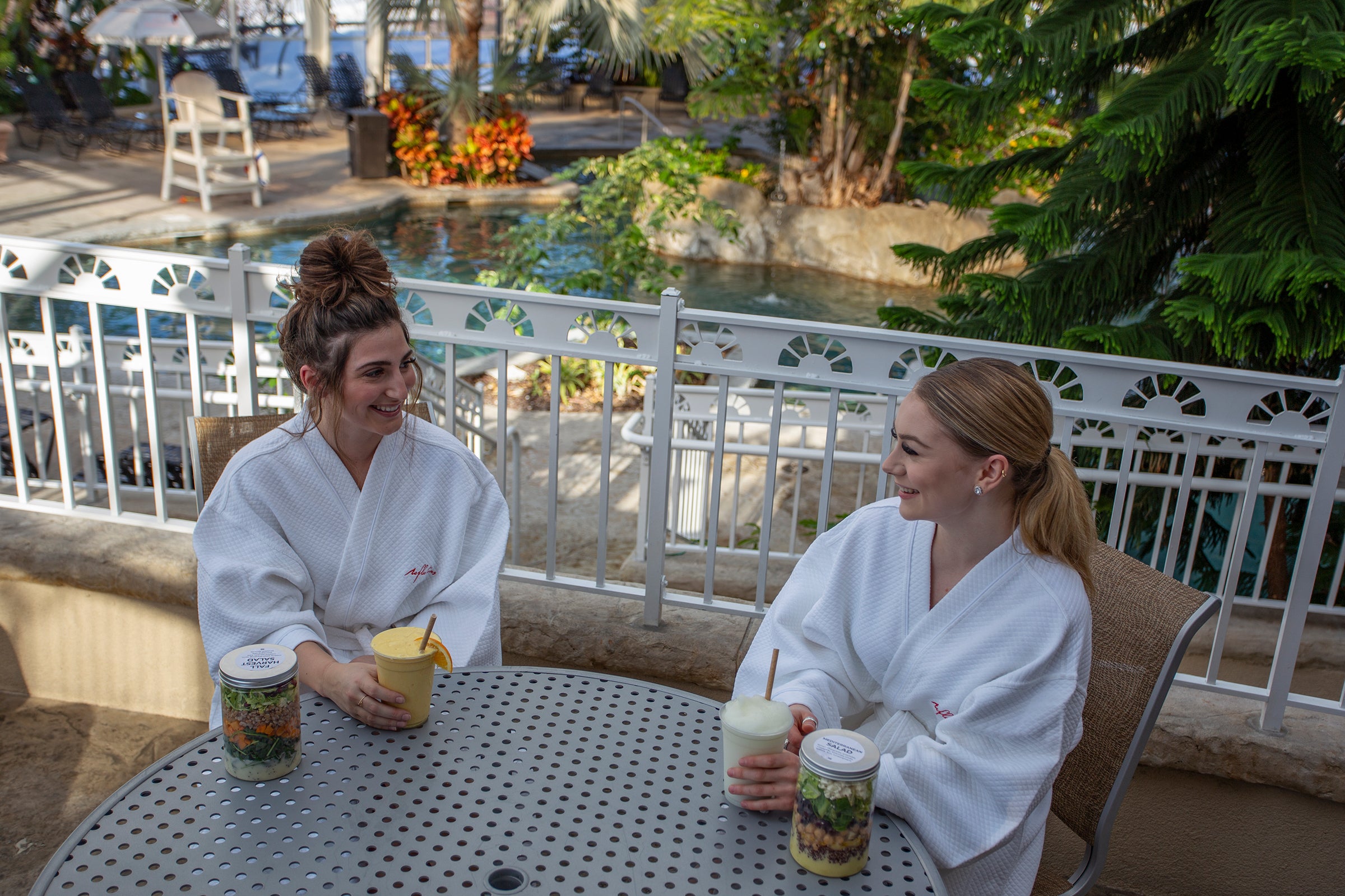 Two women sitting in white robes at a table in the Biosphere eating lunch and drinking cocktails.