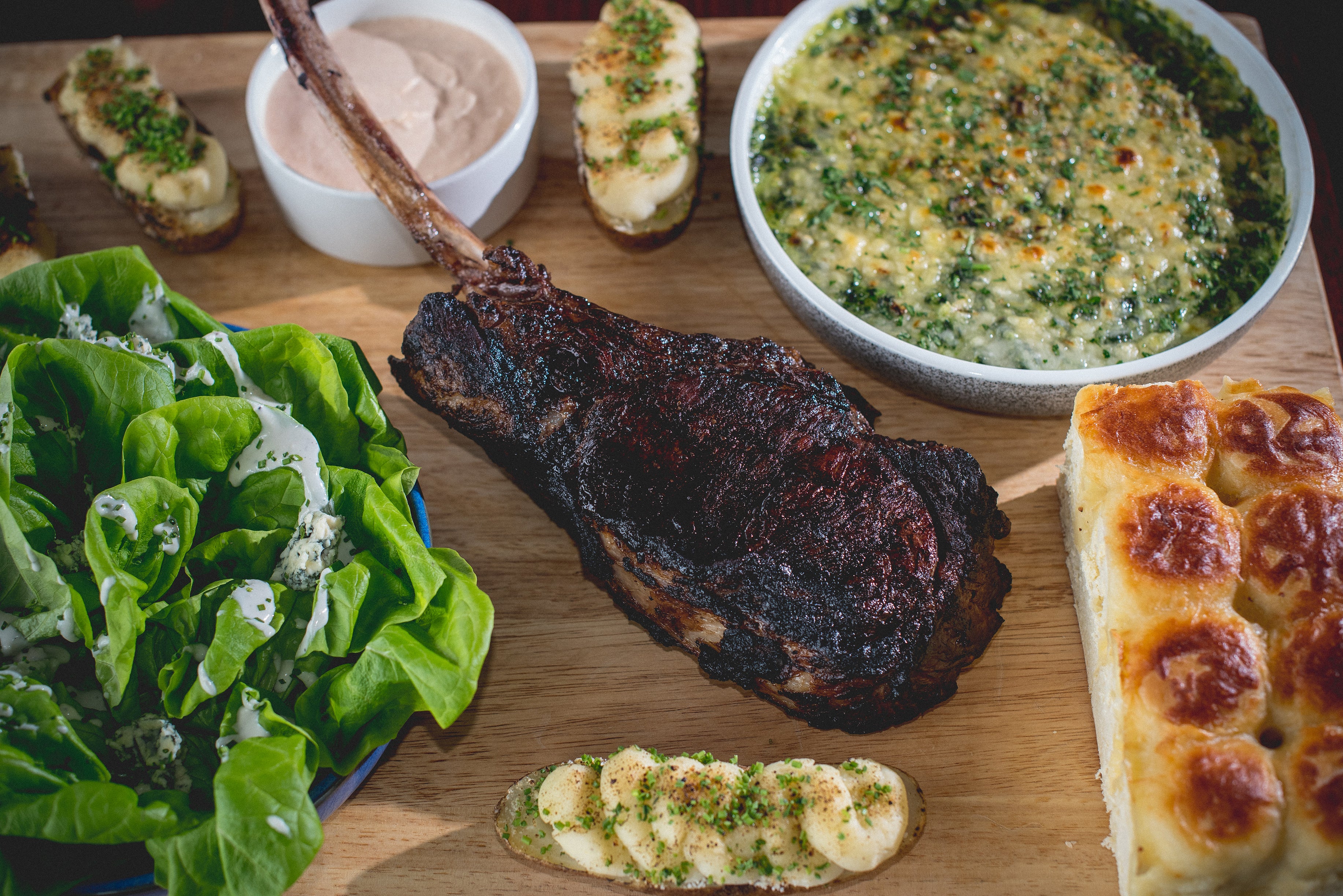 Steak, lettice, bread and more on a wooden platter.