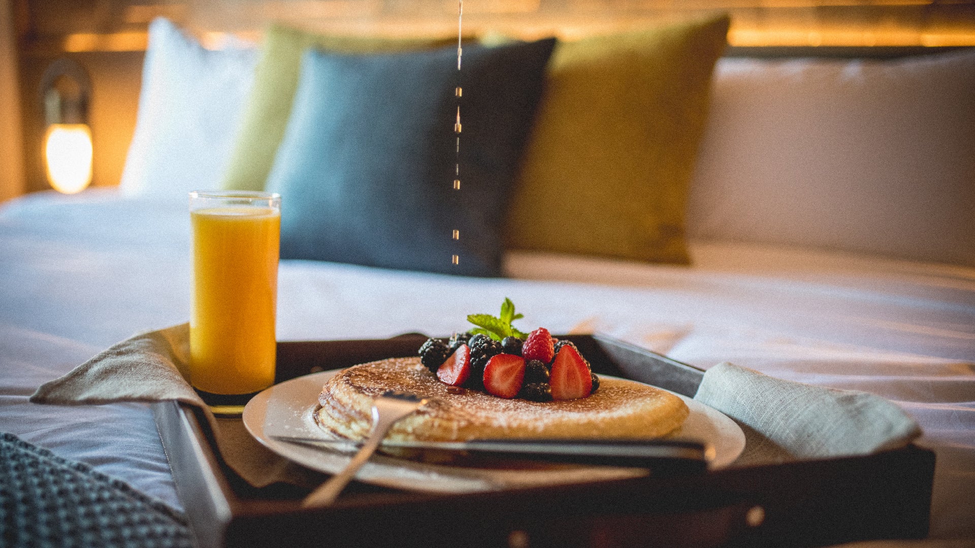 Pancales, fresh fruit and orange juice on a tray in bed.