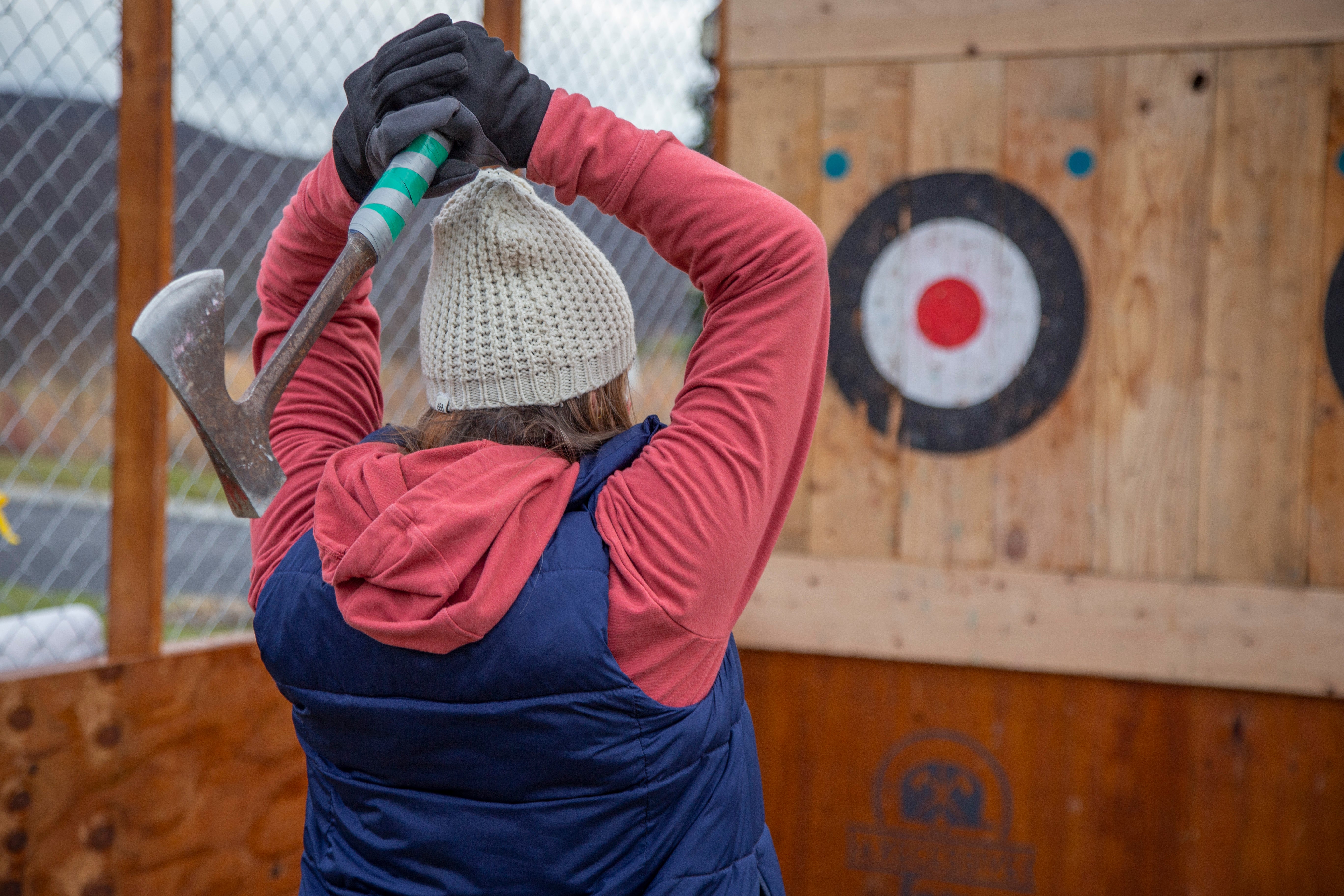 Woman wearing hat and gloves getting ready to throw axe at target.