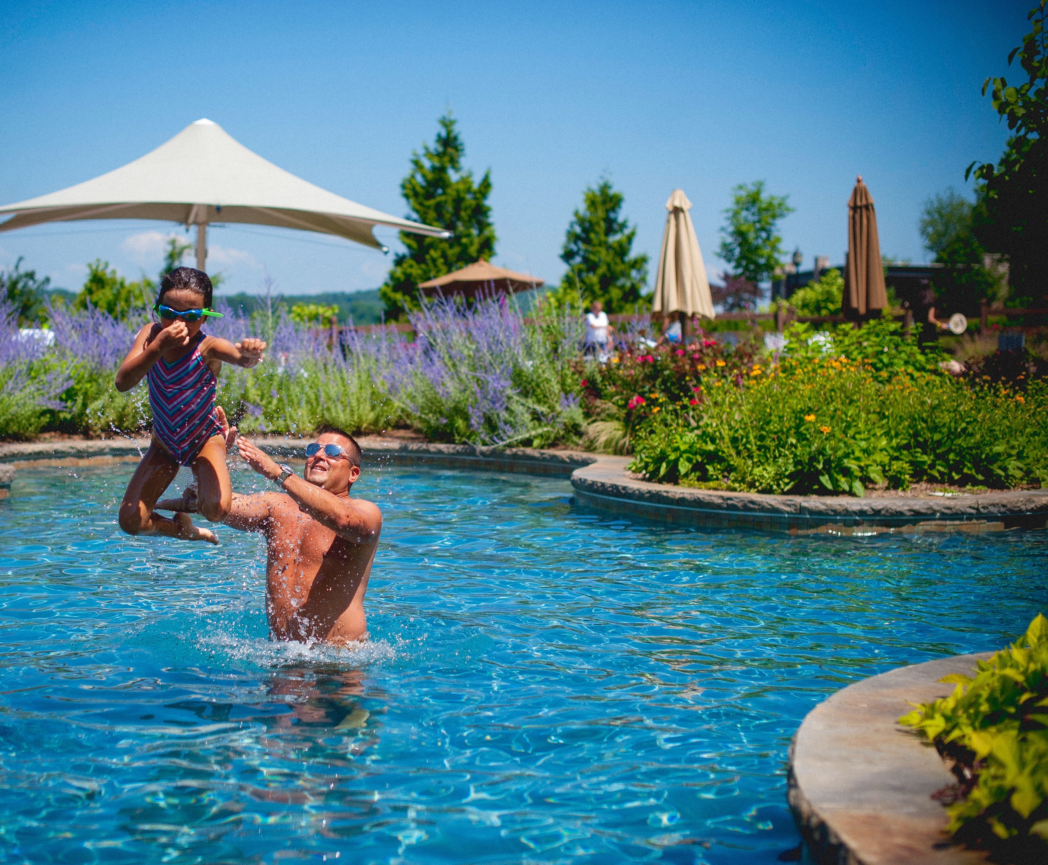 Young girl midair as her father throws her in pool.