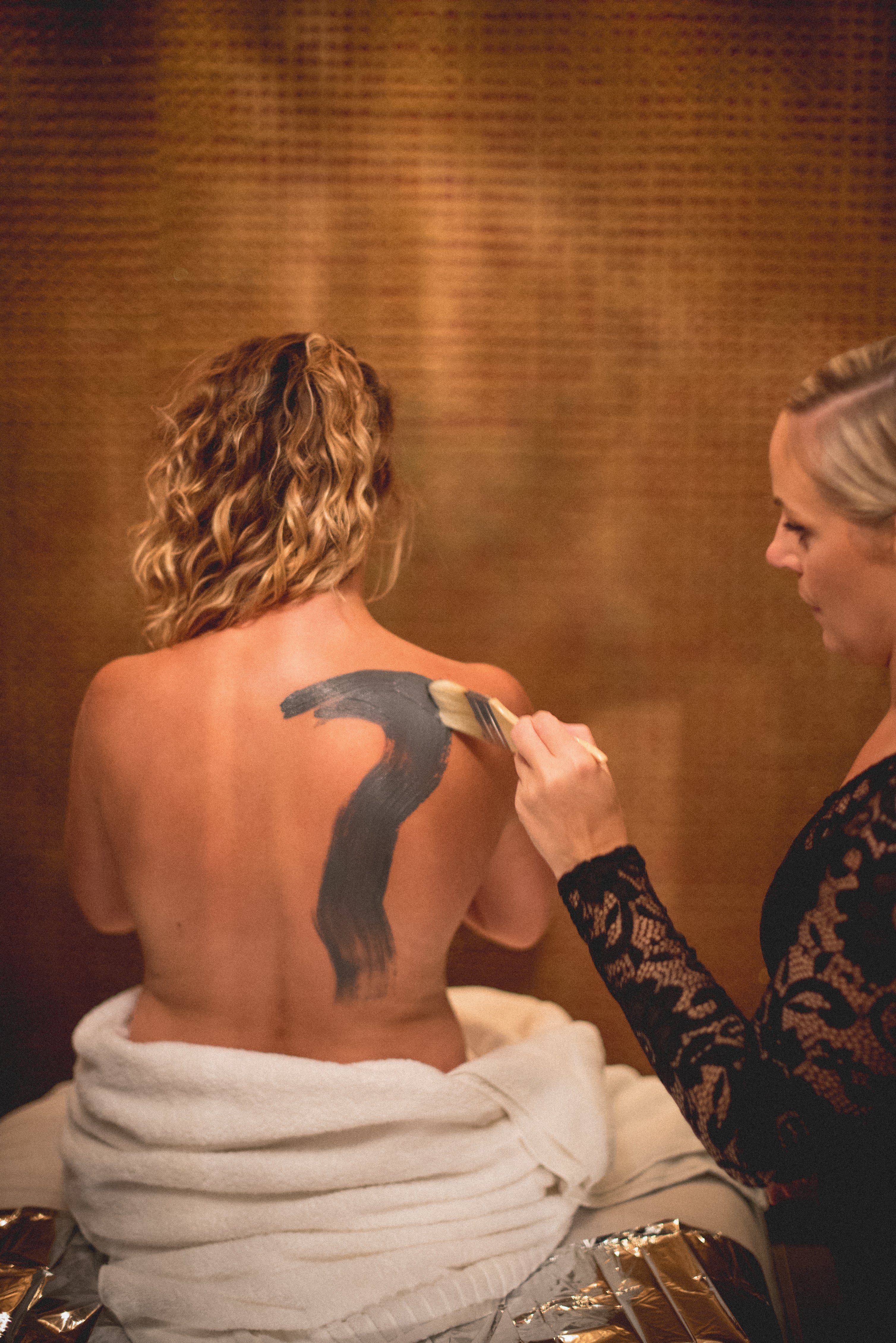 Spa therapist painting product on woman's back.