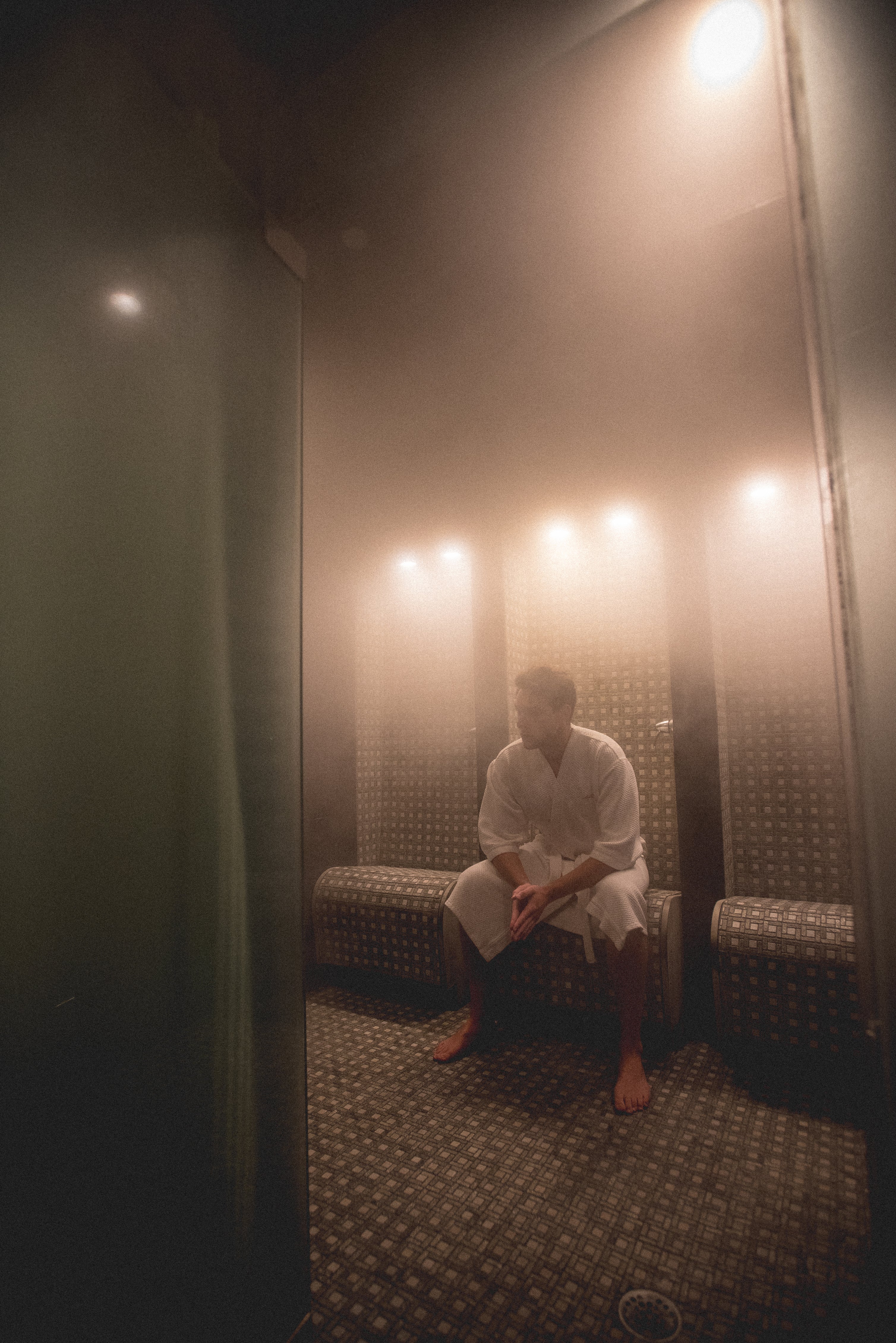 Man in white bath robe sitting in steamy sauna.