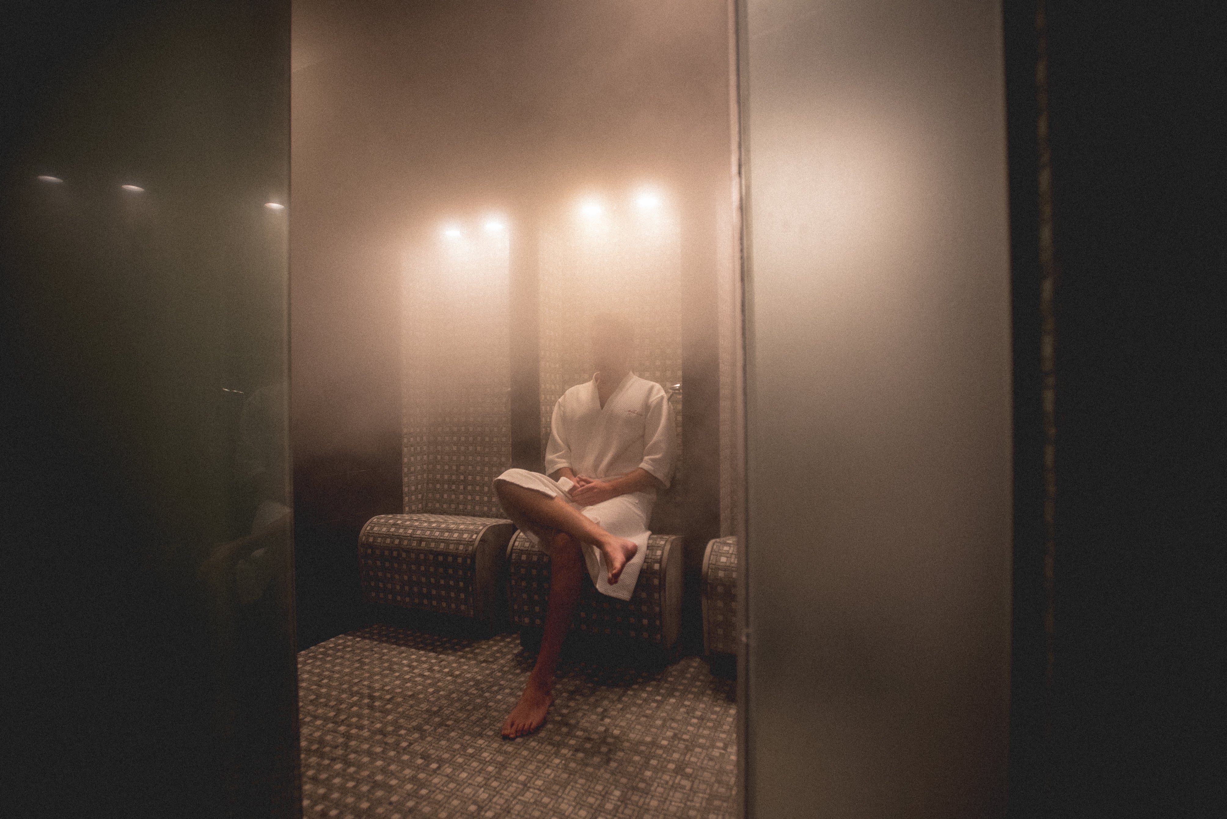 Man in white bath robe sitting in steamy sauna.