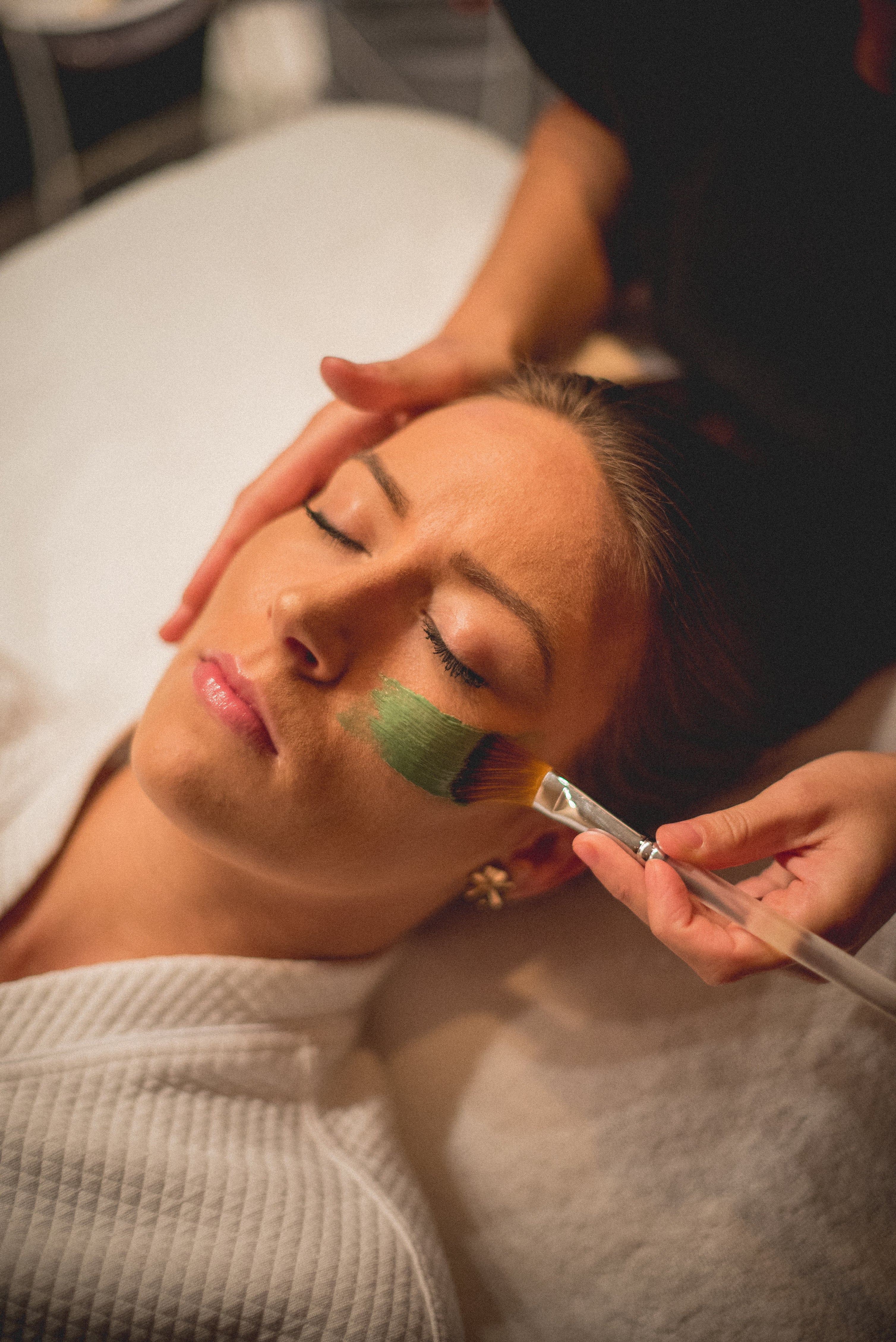 Green face mask being applied to woman's face with brush.