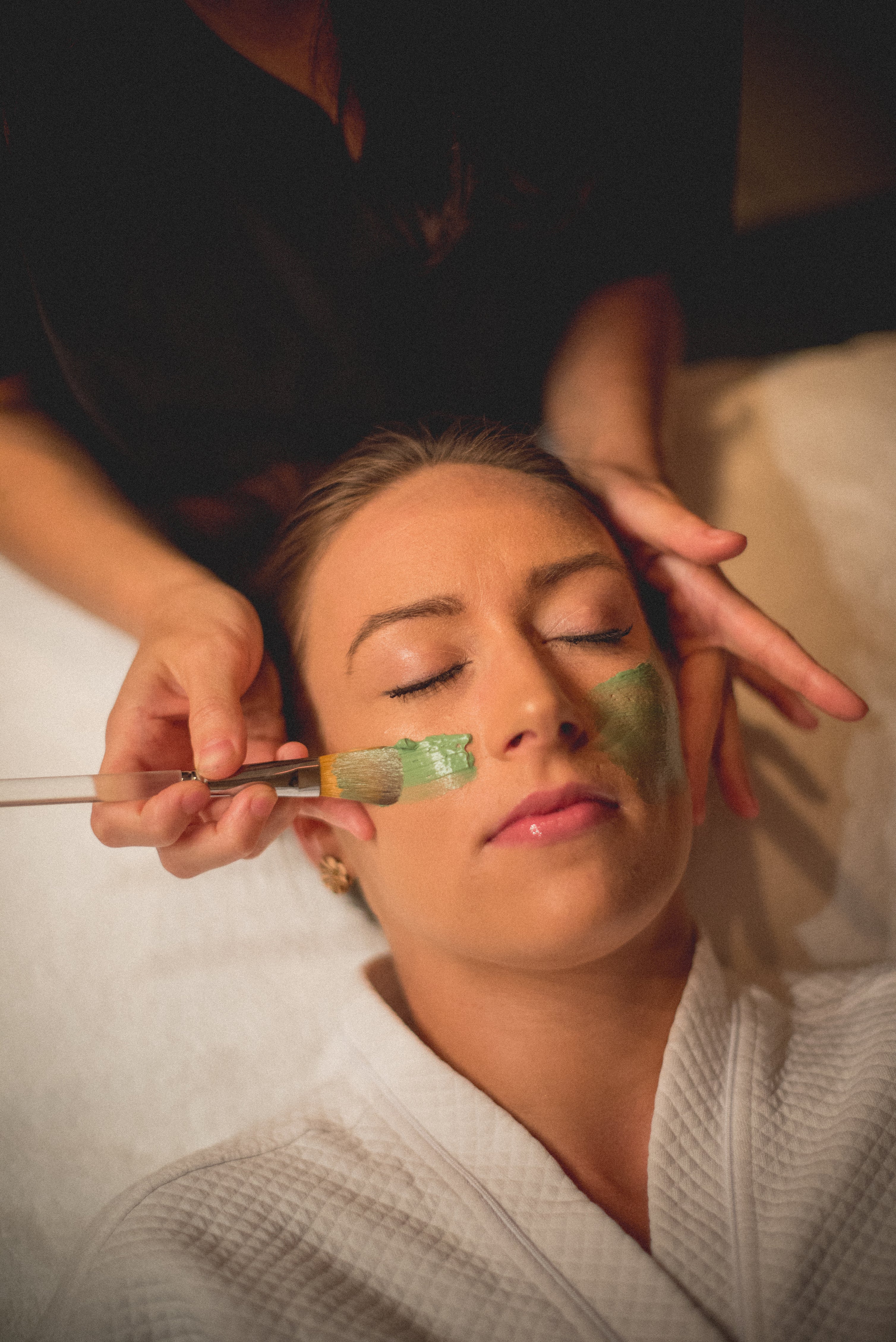 Green face mask being applied to woman's face.