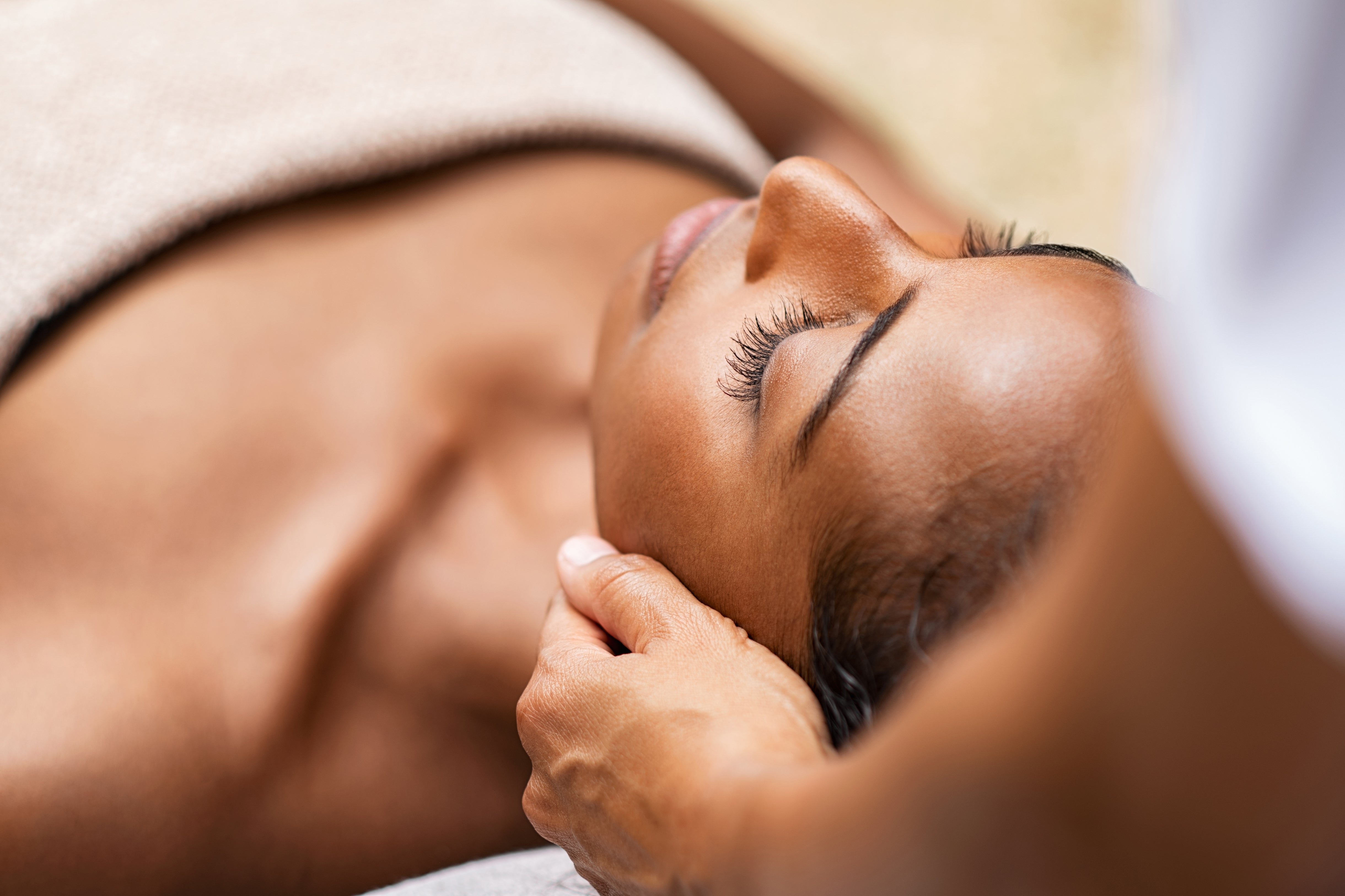 Woman laying down with tech's hands on side of her head for spa treatment.
