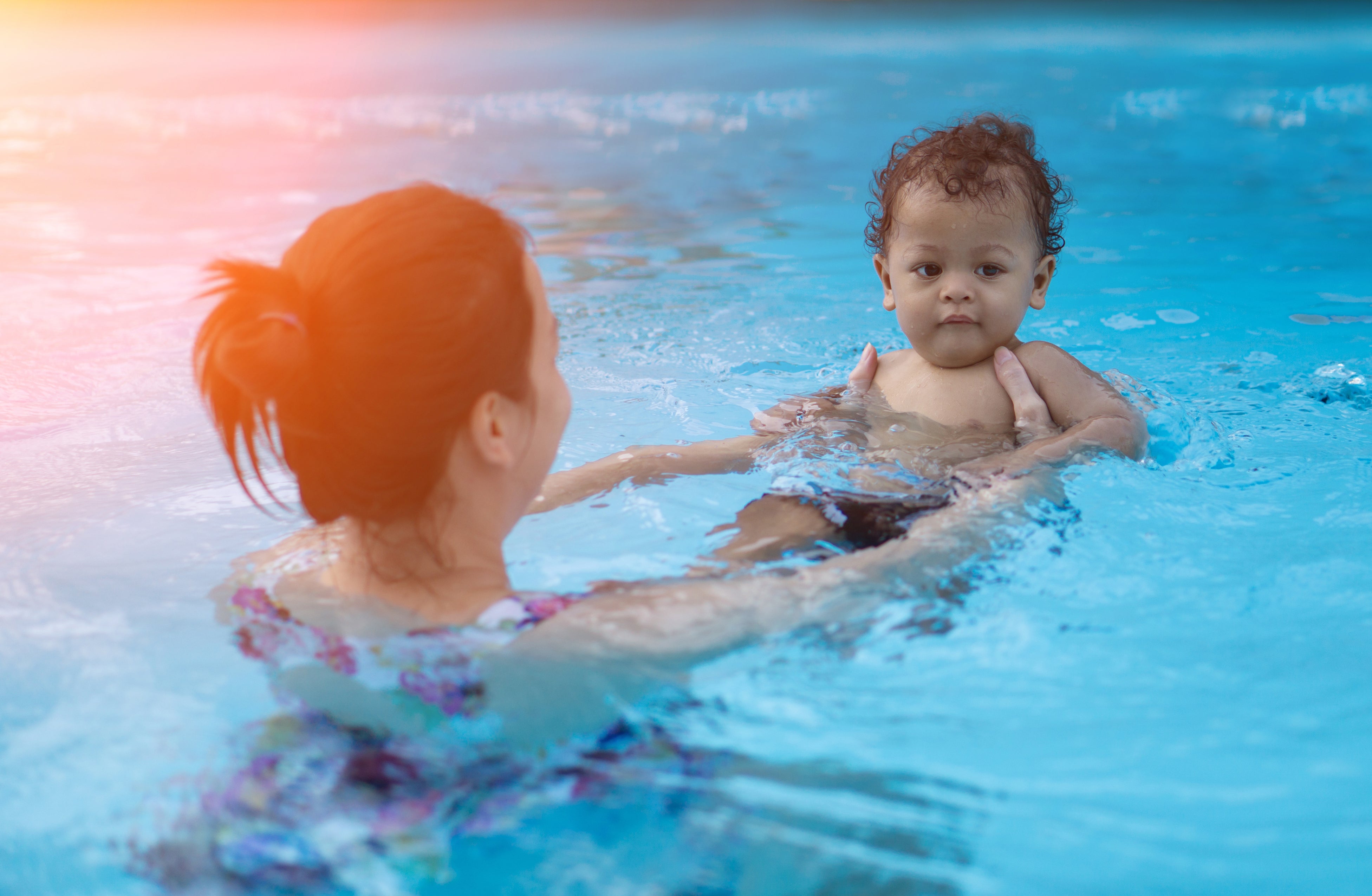 Woman holding baby in pool.