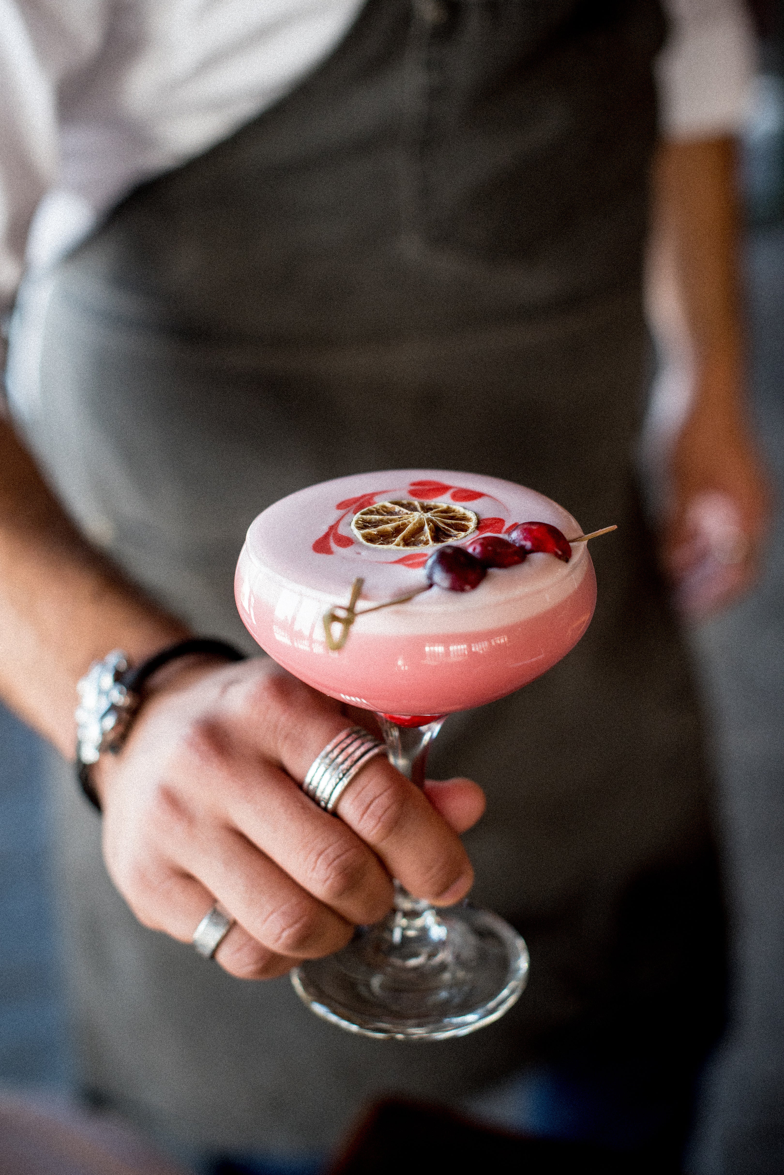 Pink cocktail in martini glass topped with blood orange and cherries.