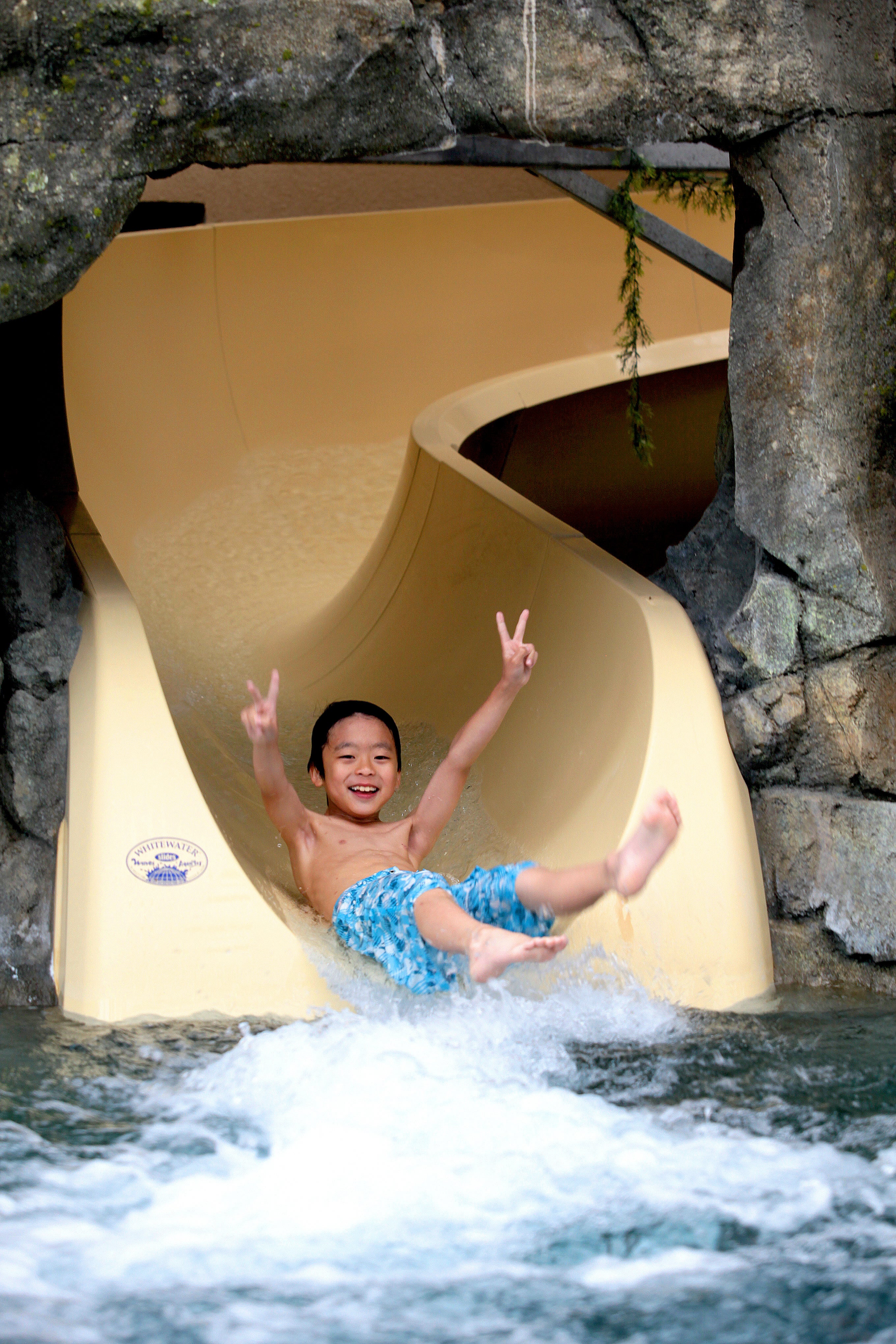 Children showing peace signs on his hands as he slides down Biosphere indoor slide.