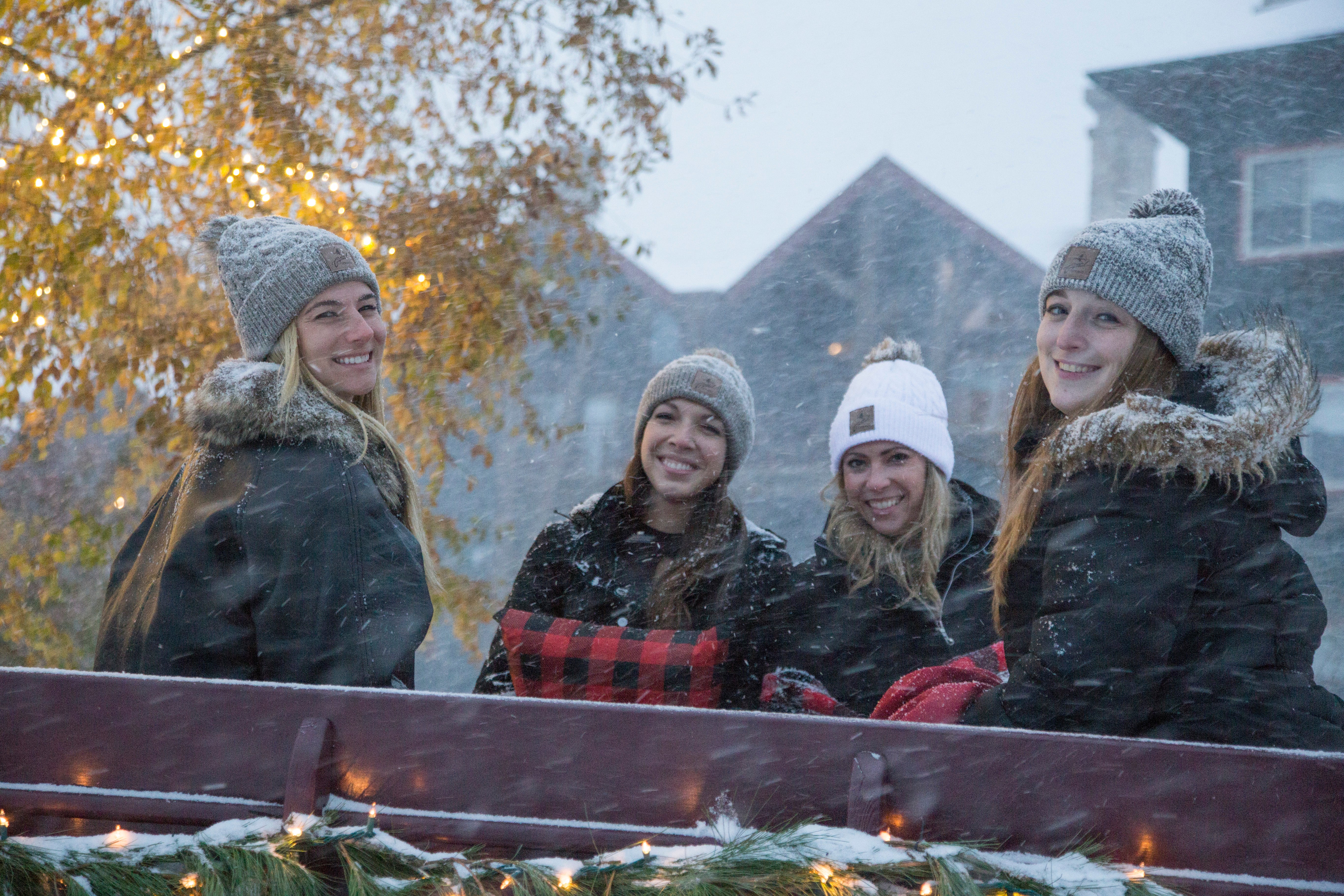 Four girlfriends sitting in a carriage while it's snowing.