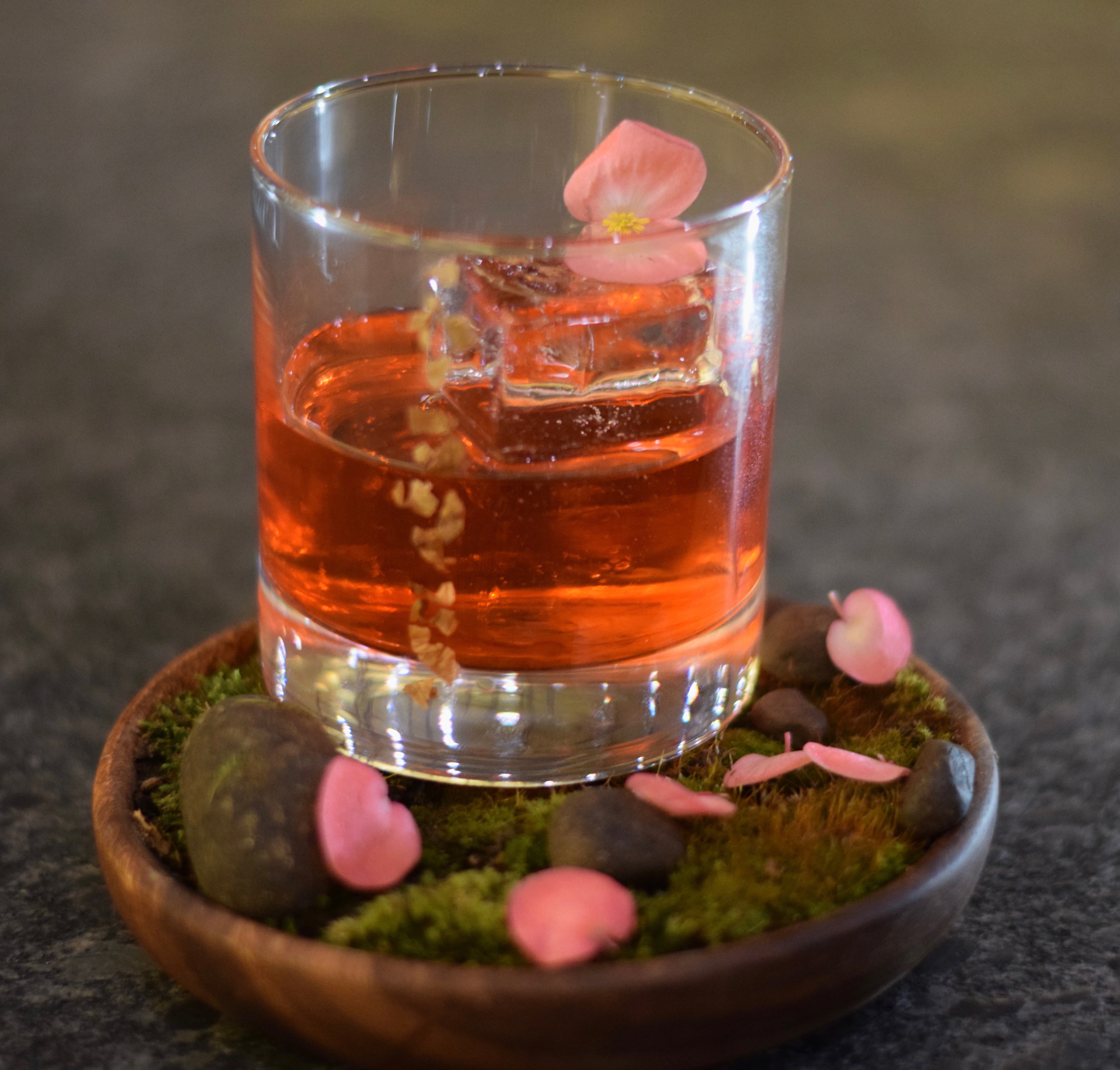 Short round glass filled with pink cocktail and flower petals.