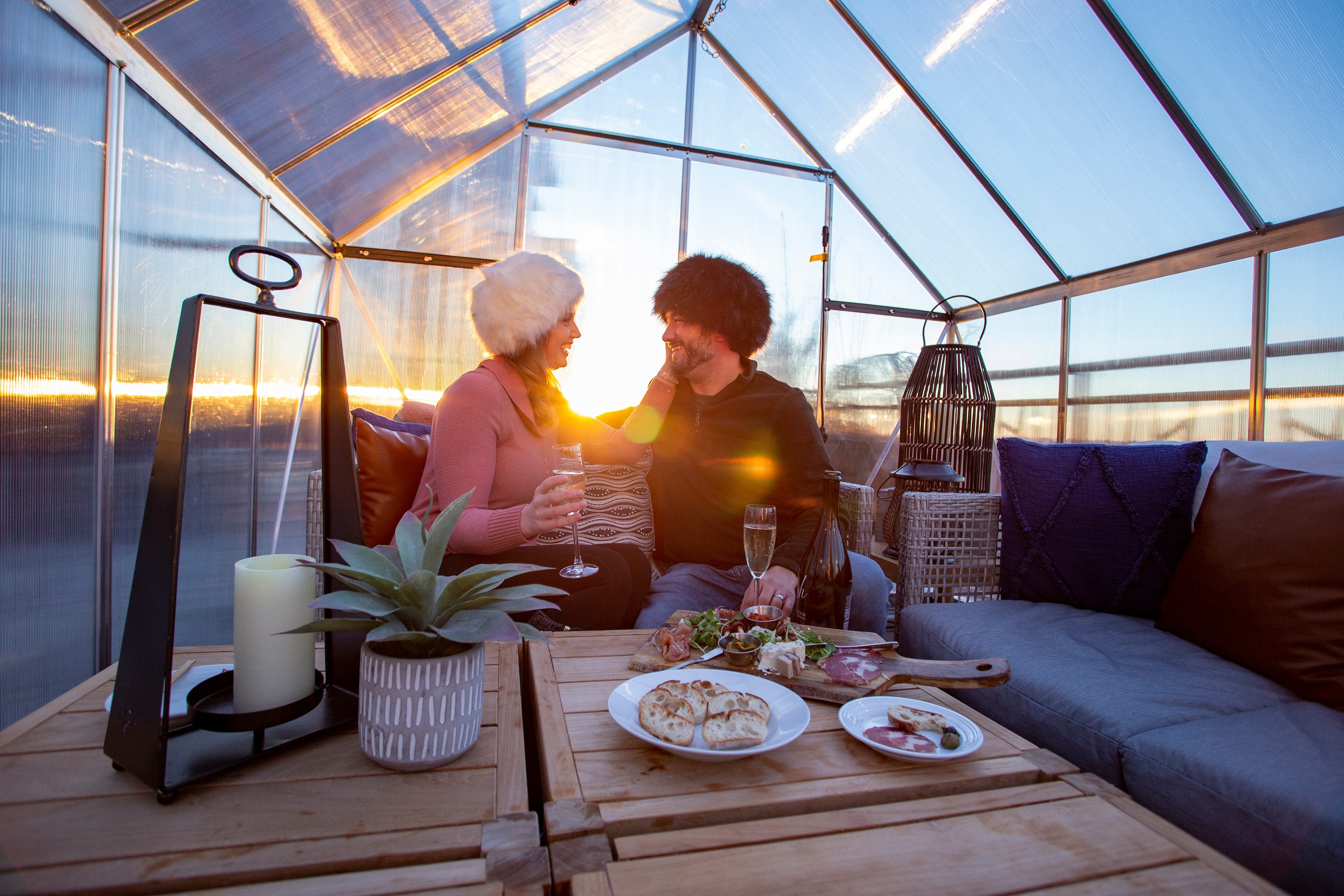 Couple in fuzzy hats drinking champagne in chalets.