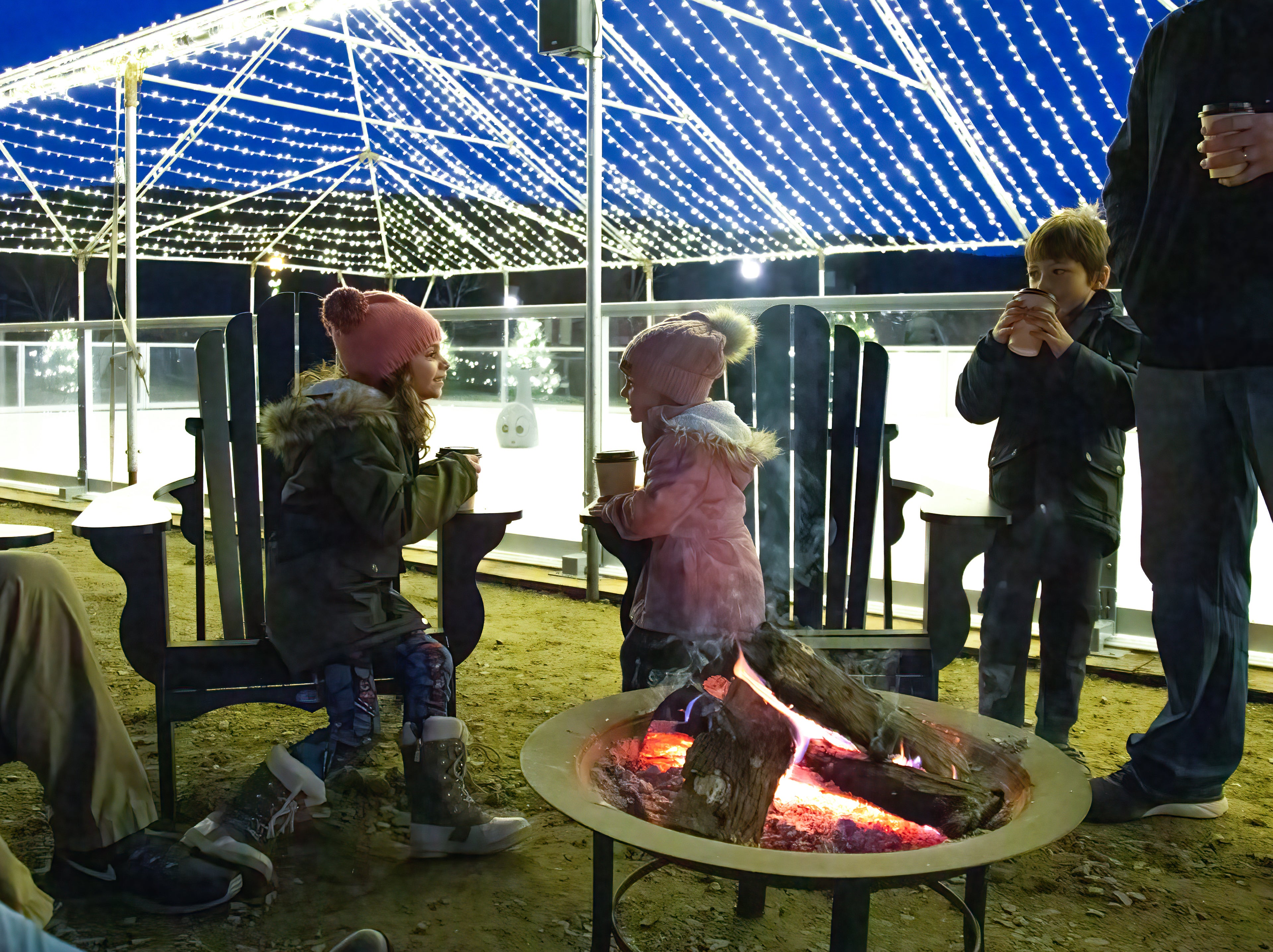Two children sitting by firepit with hot chocolate.