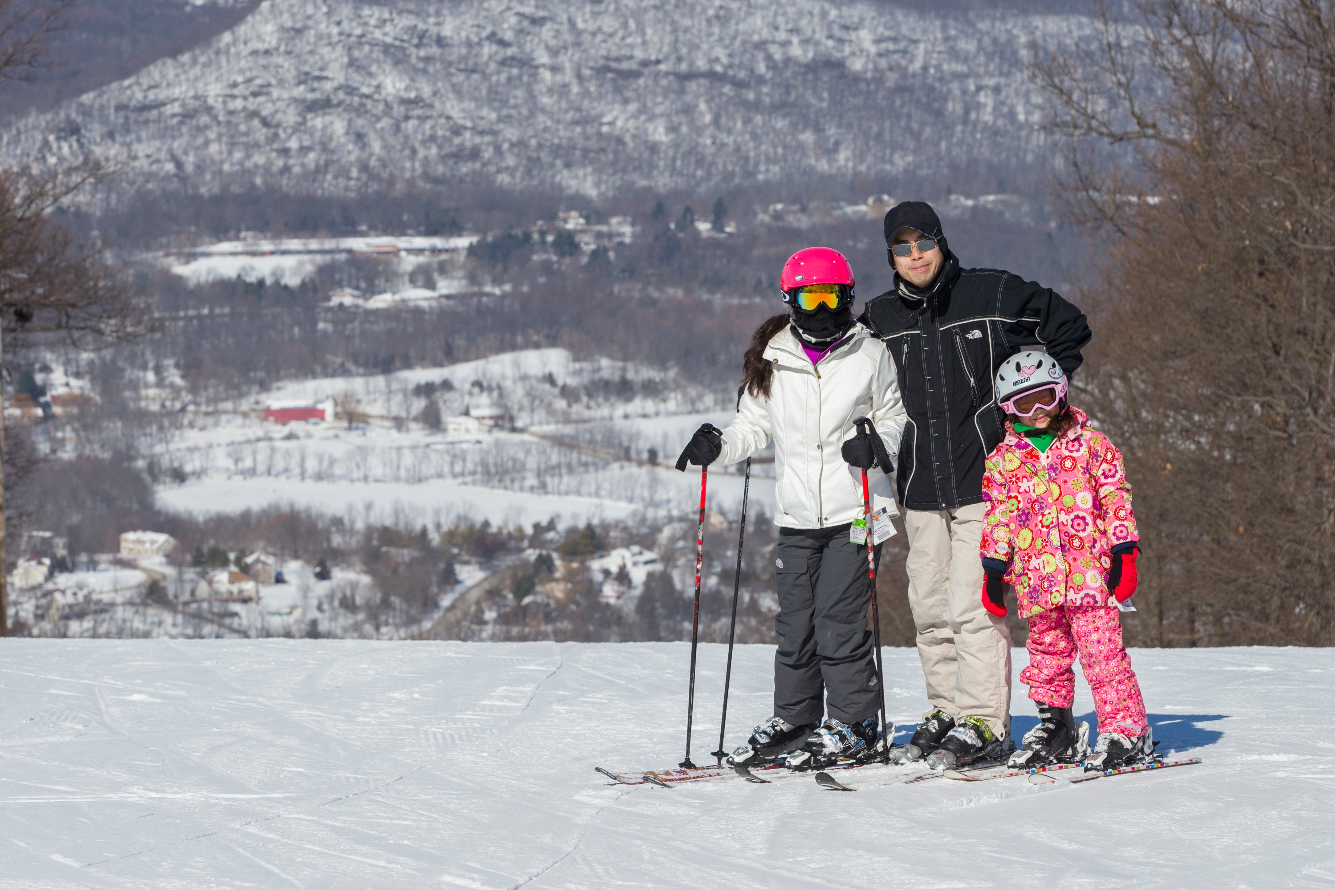 Family of 3 skiiers standing on mountain.
